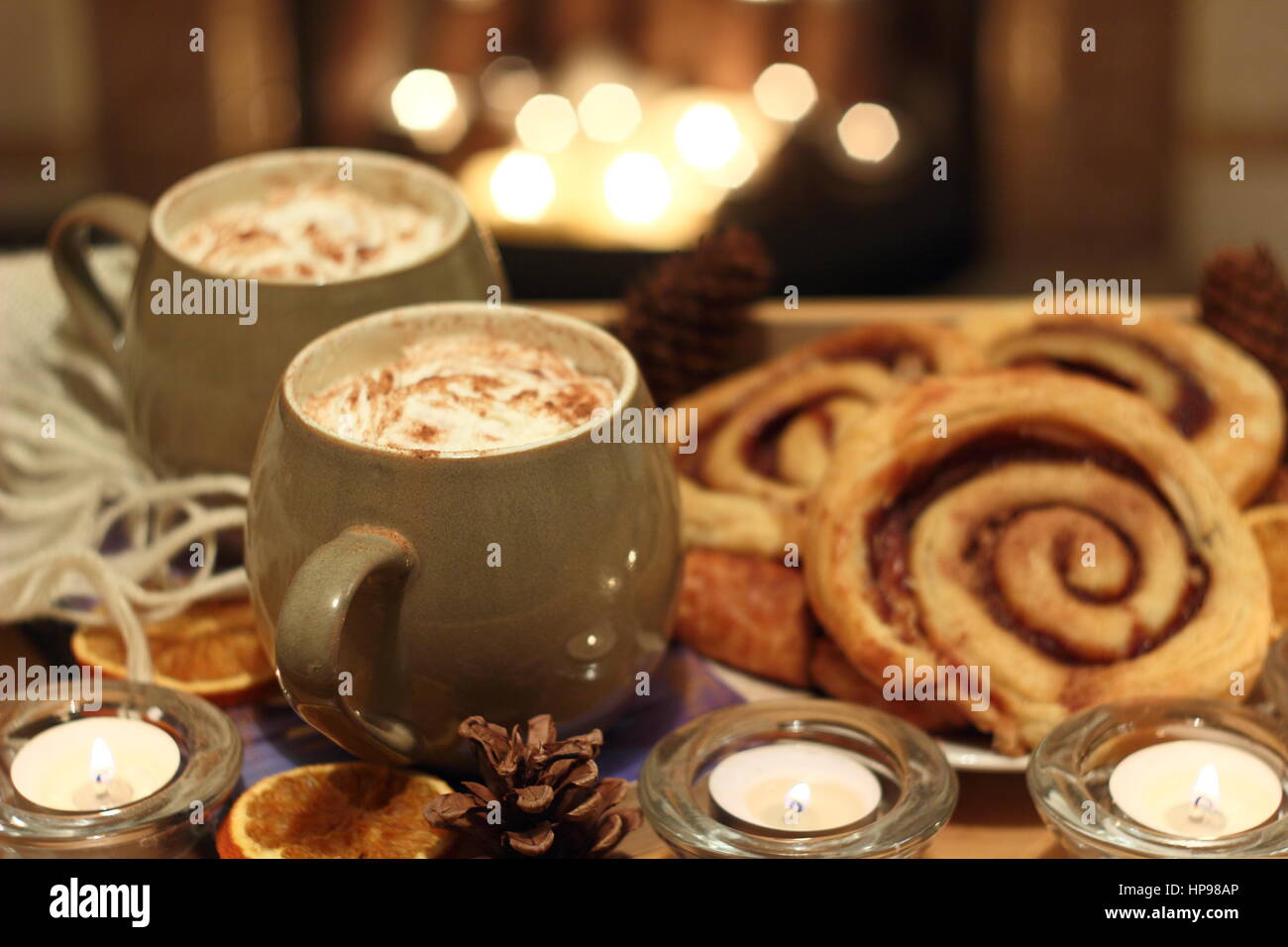 Creamy mugs of mocha - coffee and chocolate - are served with cinnamon buns by a candle lit open fireplace in a cosy English home Stock Photo