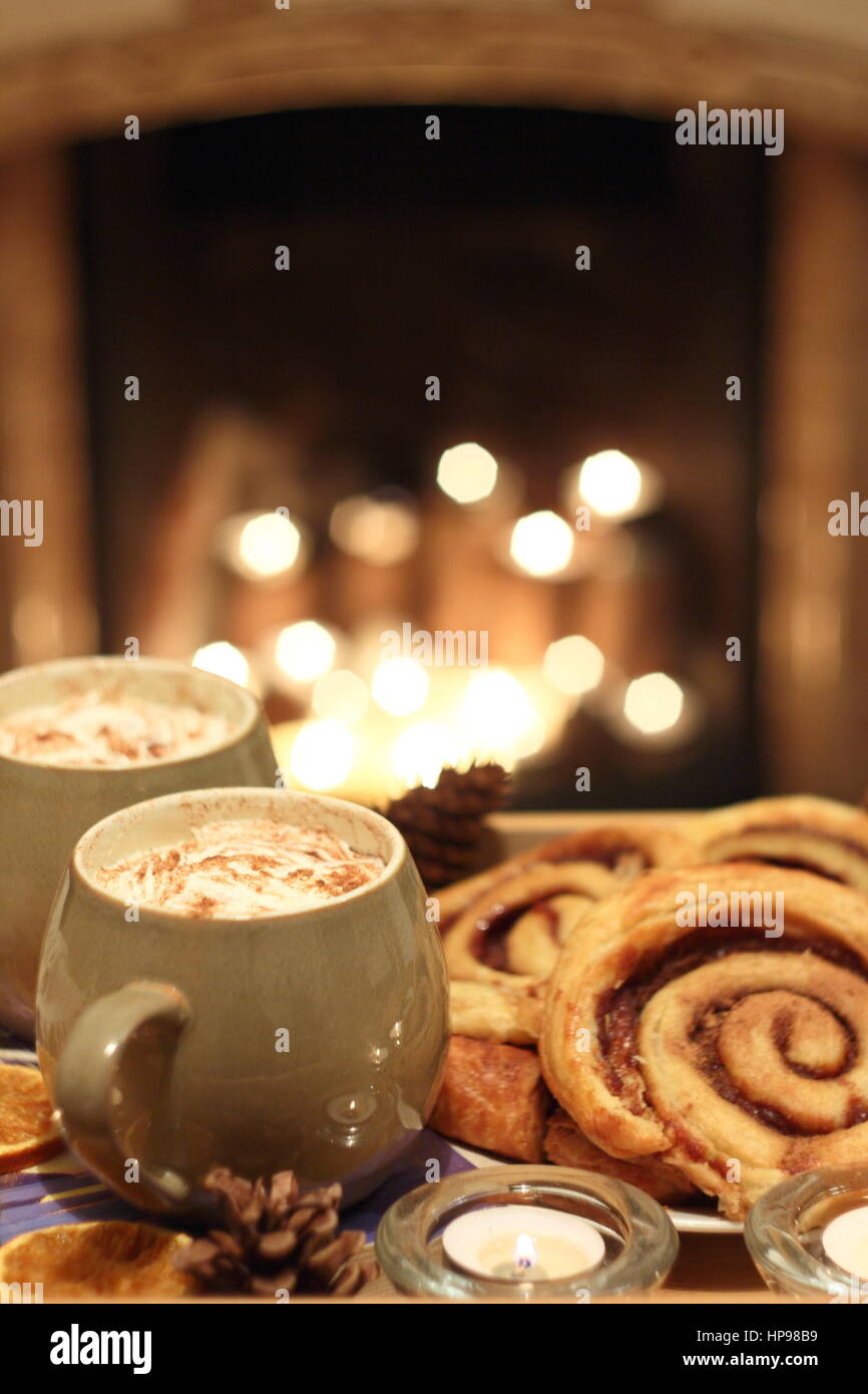 Creamy mugs of mocha - coffee and chocolate - are served with cinnamon buns by a candle lit open fireplace in a cosy English home Stock Photo