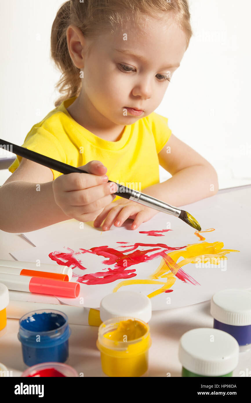 Cute little toddler child painting with paintbrush and colorful paints. Adorable baby girl drawing, sitting behind table, isolated on white background Stock Photo