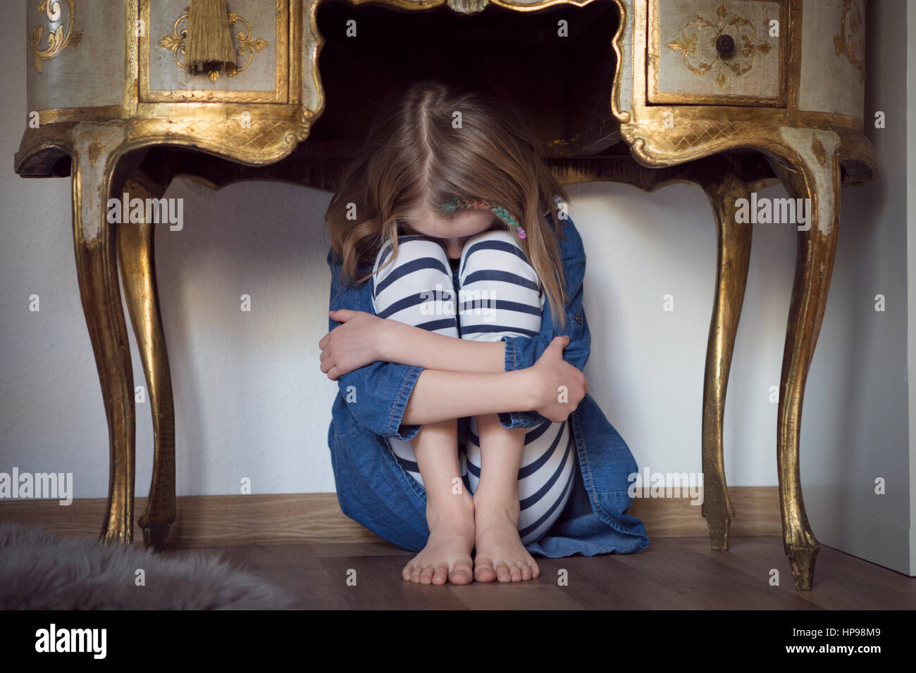 Child hiding under table in fear Stock Photo
