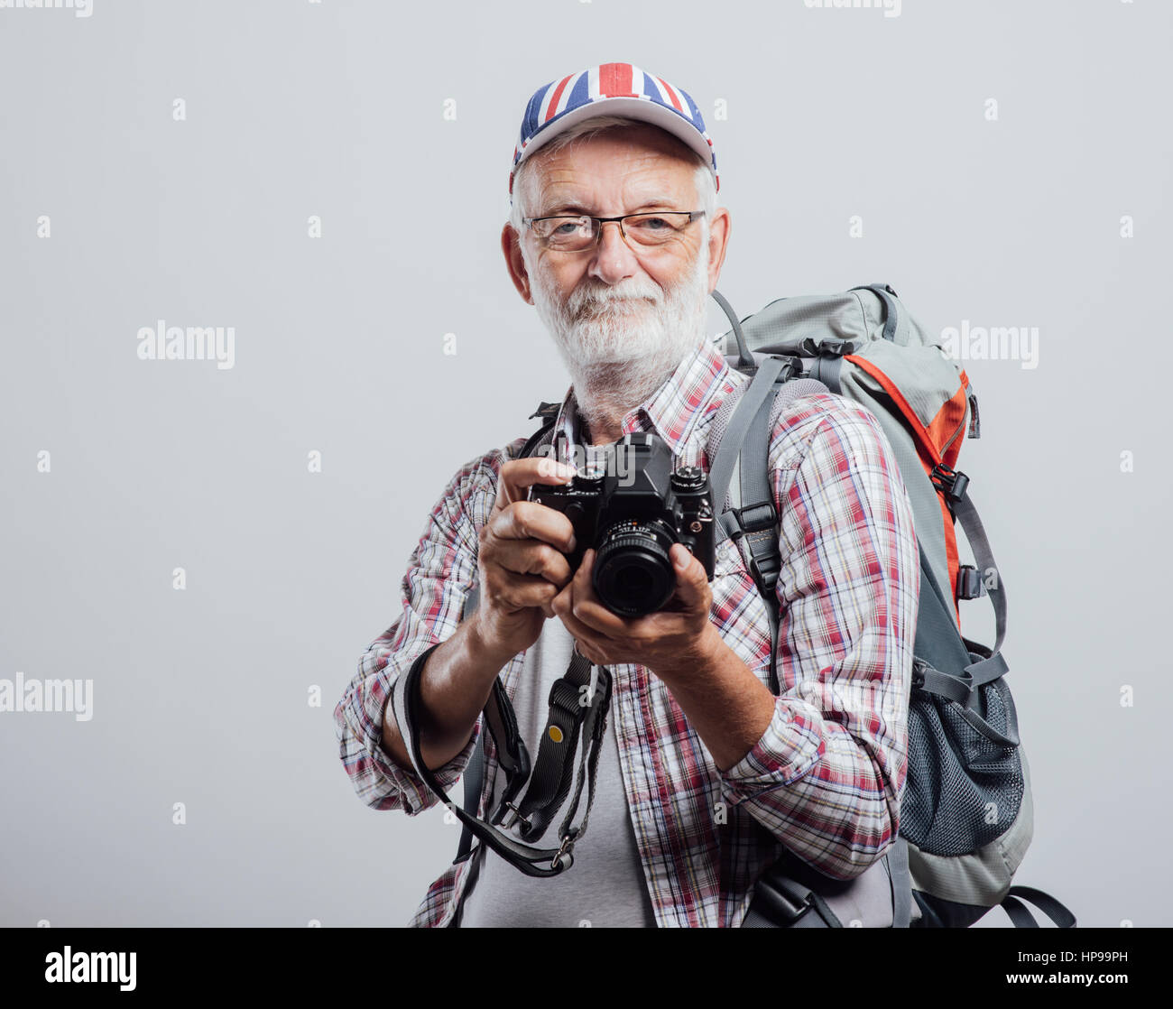 Senior tourist photographer with backpack and digital camera, he is wearing a British flag cap Stock Photo