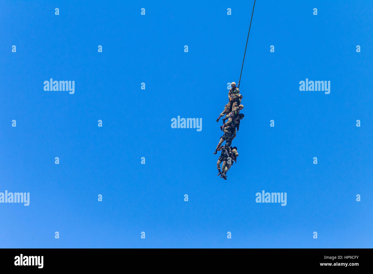 Soldiers attached to rope flying airlift below helicopter military