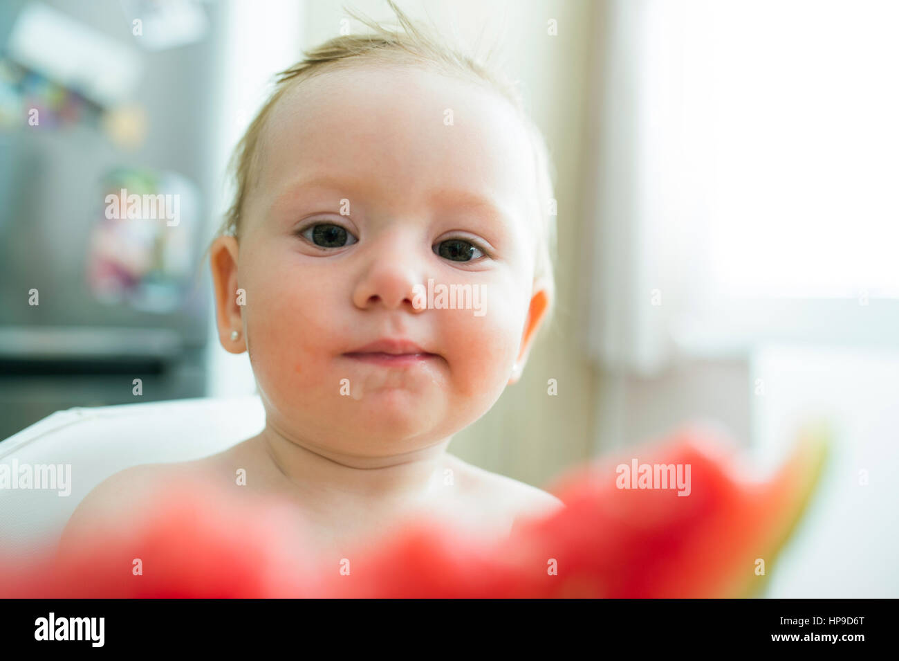 Cute little girl sitting in high chair eating watermelon Stock Photo