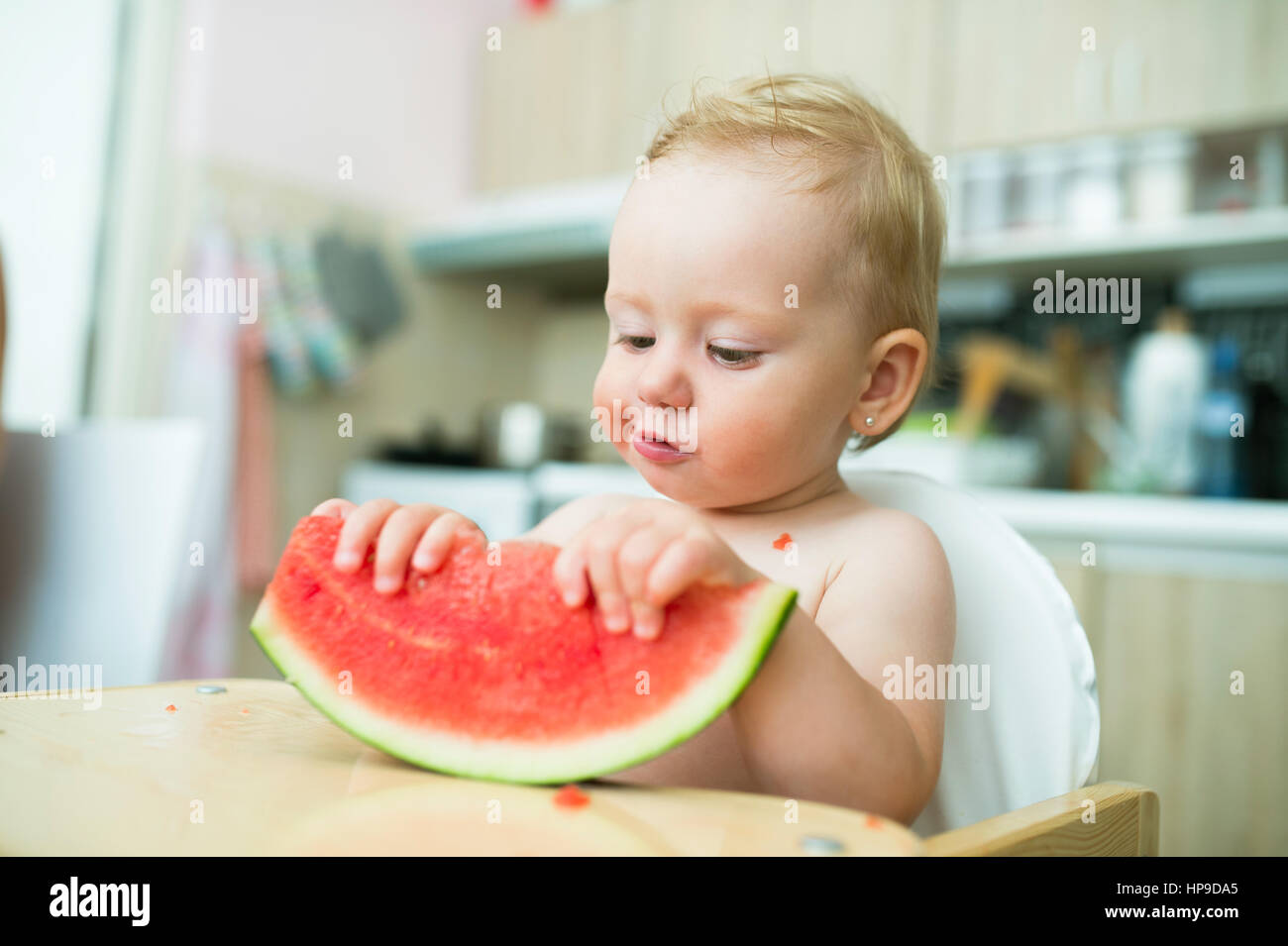 Cute little girl sitting in high chair eating watermelon Stock Photo