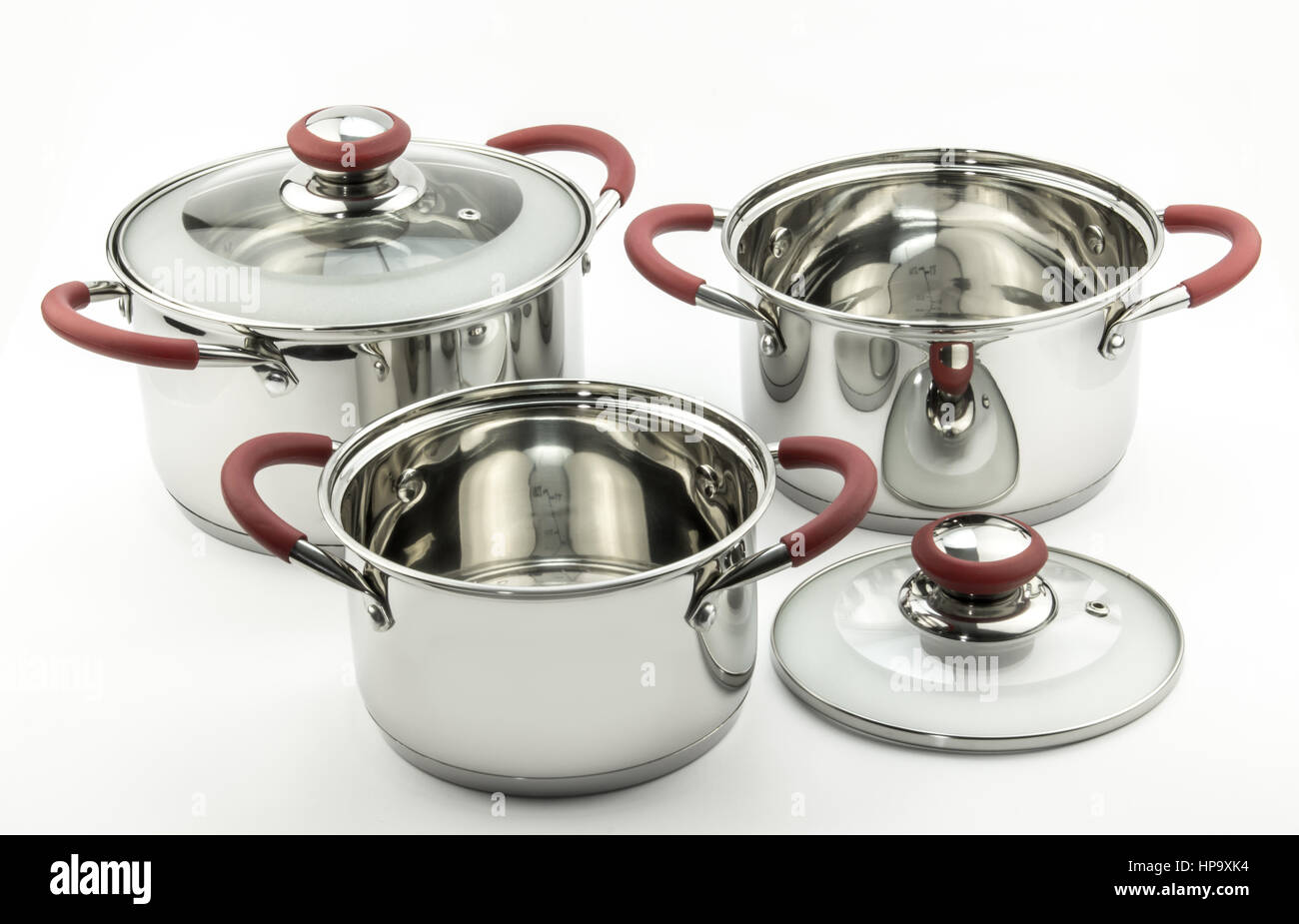 Three kitchen cooking pots with red handles and glass lids isolated on