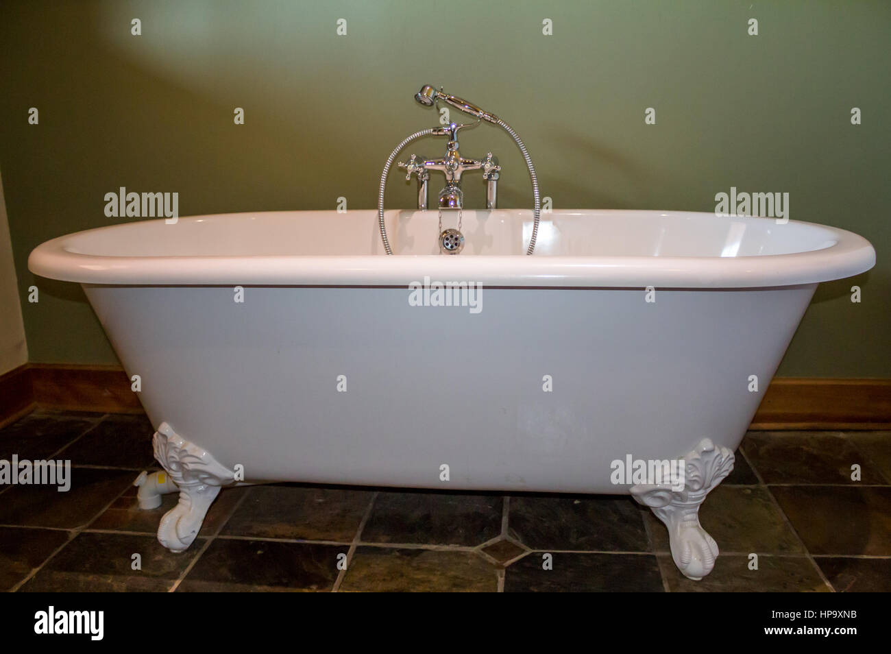 Vintage type footed white bath tub in olive green bathroom with slate tile floor Stock Photo