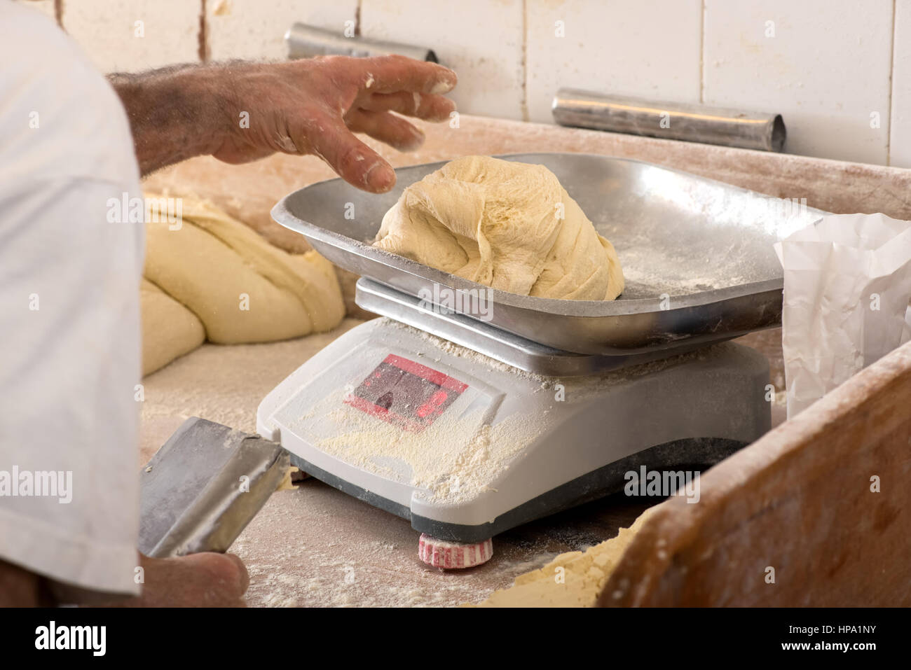 Close-up man hands weighting piece of dough on scales in bakery, flour is everywhere Stock Photo
