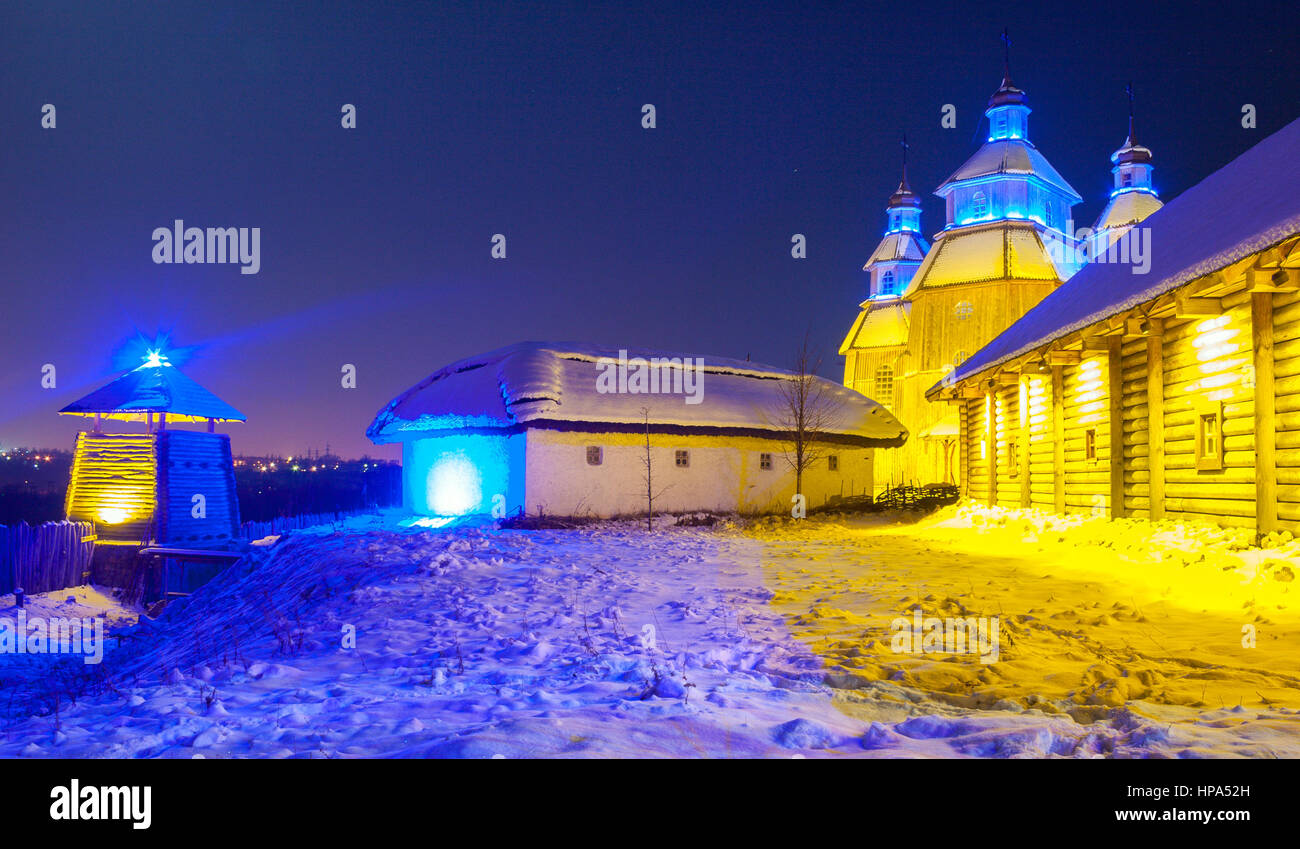Winter night on cossacks fortress 'Zaporizka Sich' with illuminated wooden church and buildings, Khortytsia island, Zaporozhye, Ukraine Stock Photo