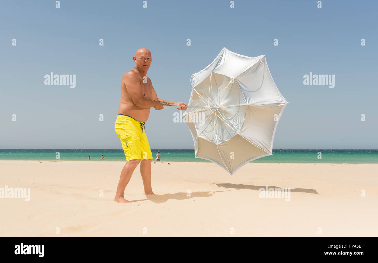 Man with sun umbrella on a windy day. Tarifa, Costa de la Luz, Cadiz, Andalusia, Spain. Stock Photo
