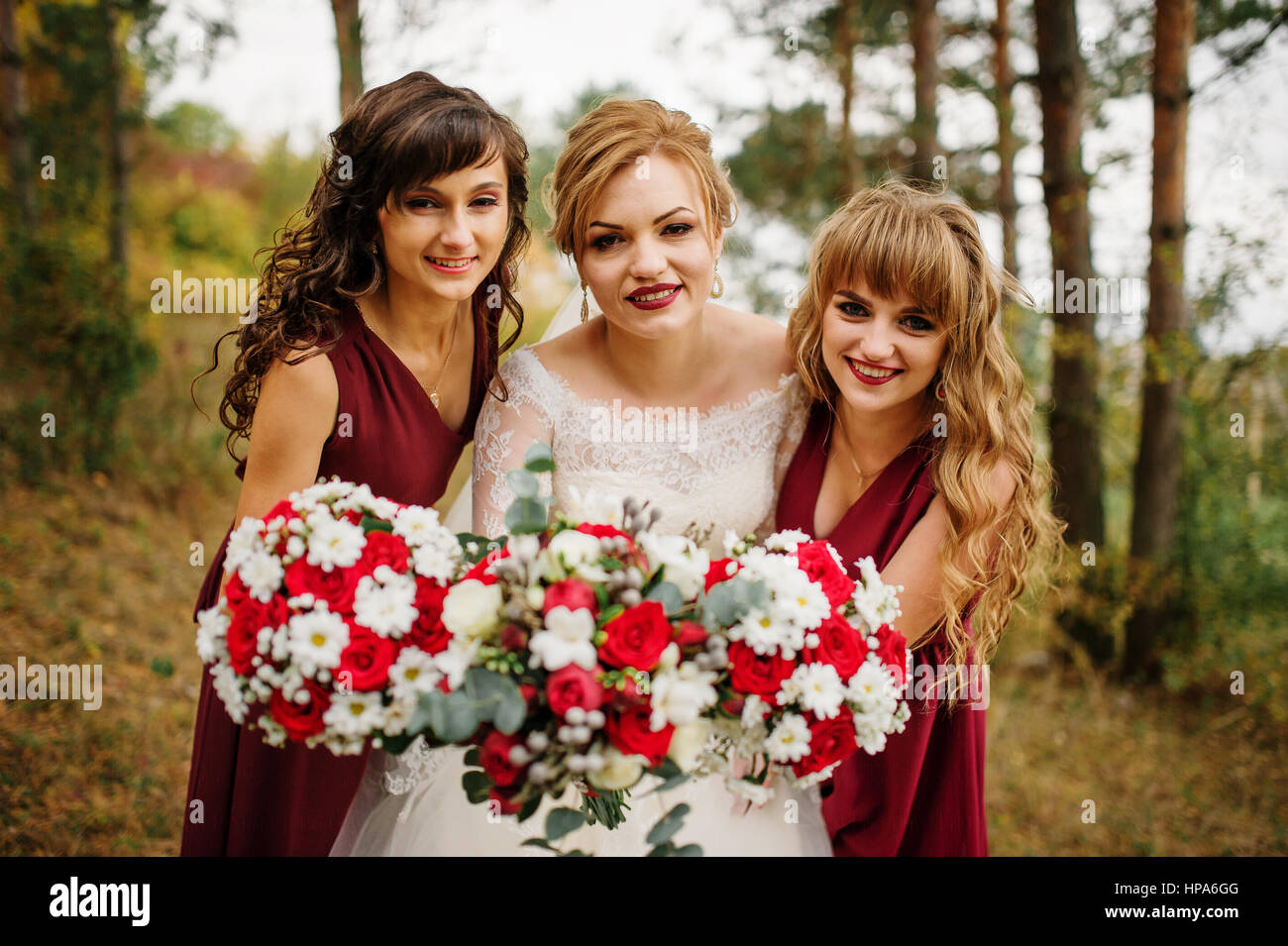 Bride with bridesmaids on red dresses at autumn pine wood Stock Photo ...
