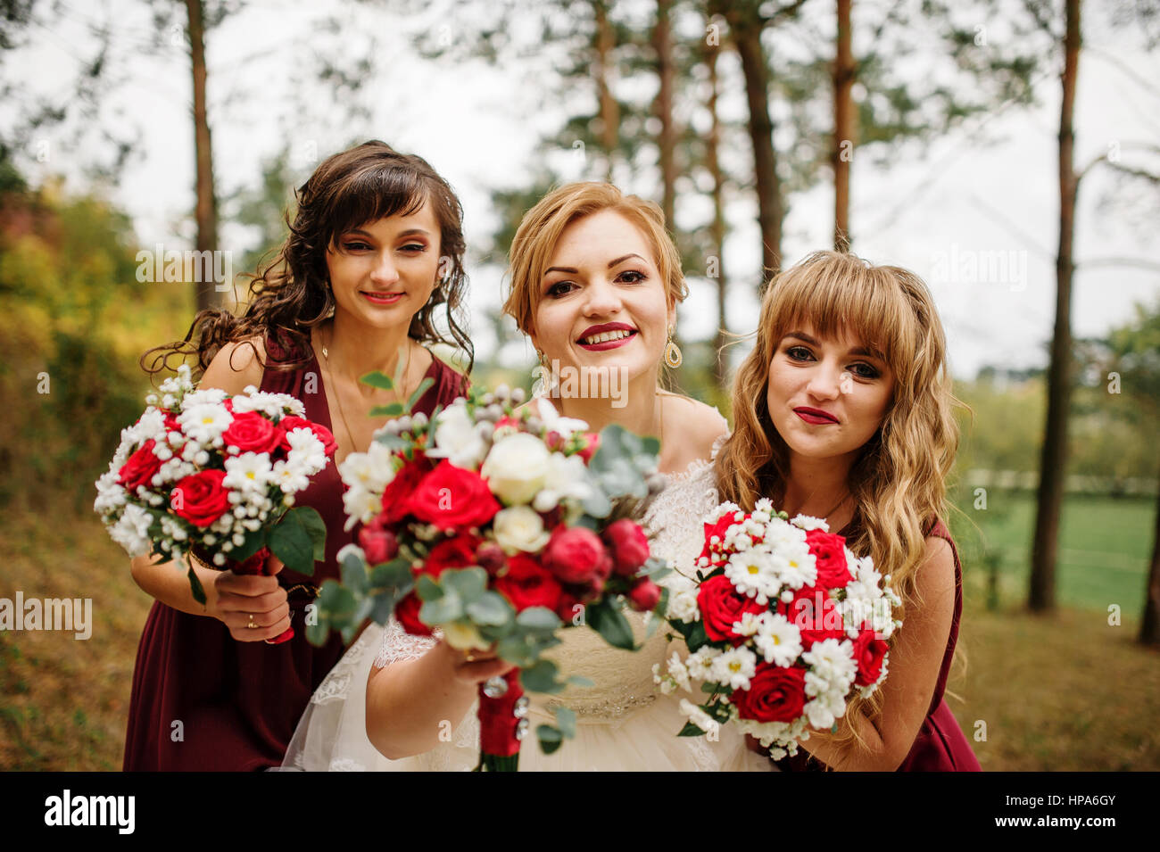 Bride with bridesmaids on red dresses at autumn pine wood Stock Photo ...