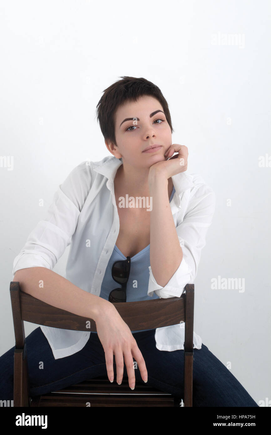 Young beautiful sexy smiling girl in shirt sitting on chair isolated on the white background, looking at the camera. Stock Photo