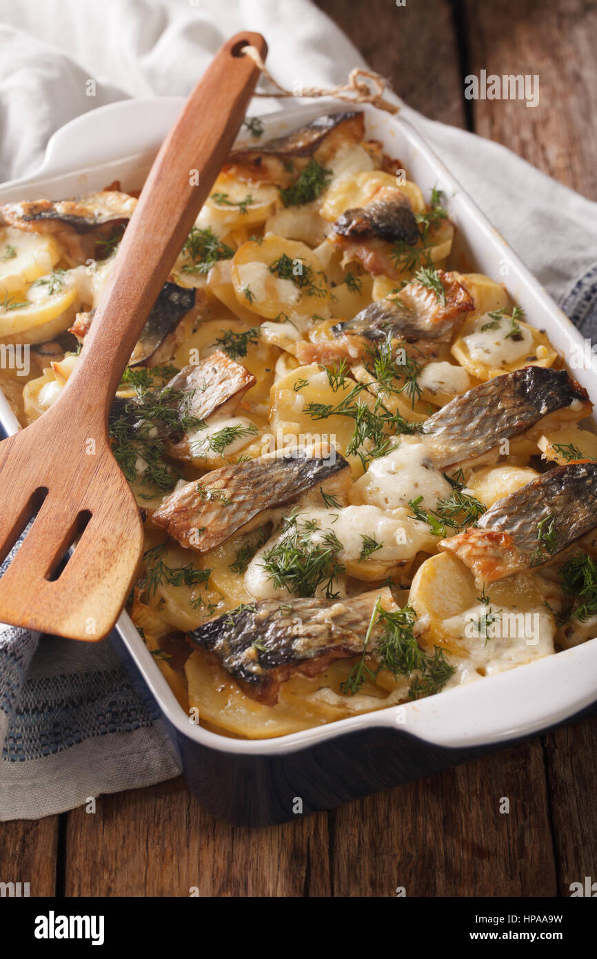 casserole of potatoes, herring fish in a creamy sauce close up in baking dish on the table. vertical Stock Photo