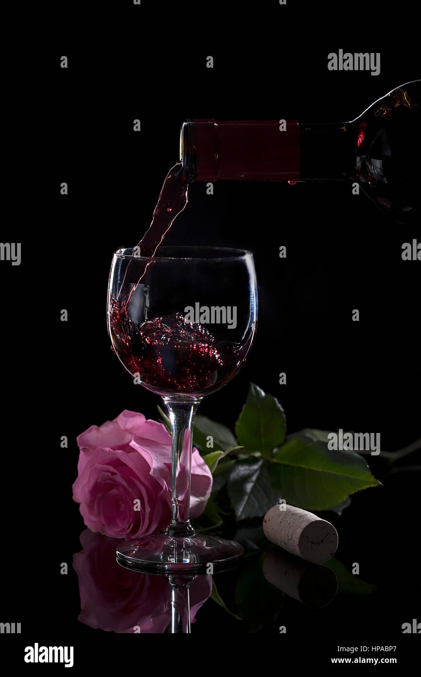 A studio image of pouring wine into a wine glass by a pink rose. Stock Photo