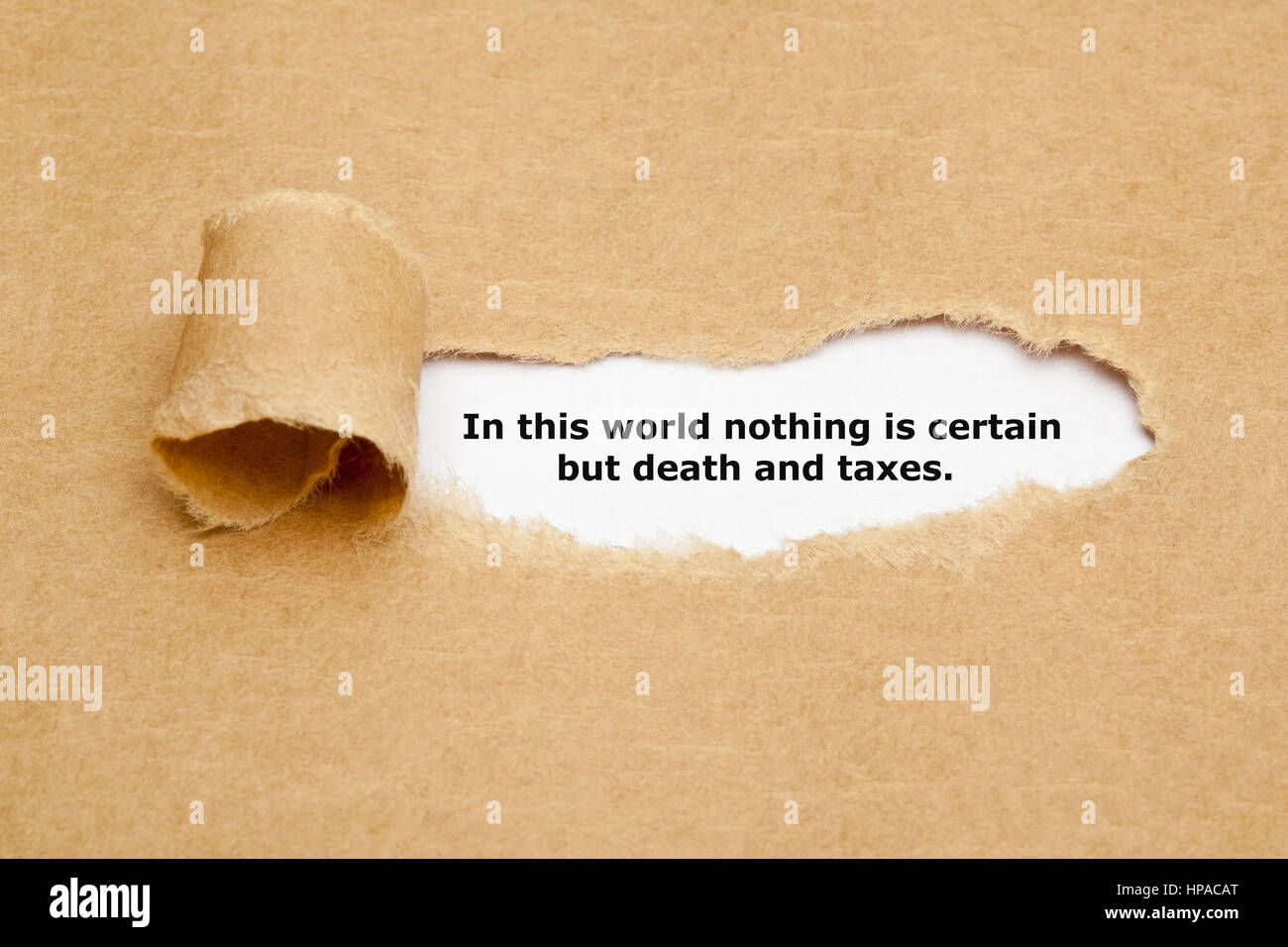 Quote In this world nothing is certain but death and taxes, appearing behind ripped brown paper. Stock Photo