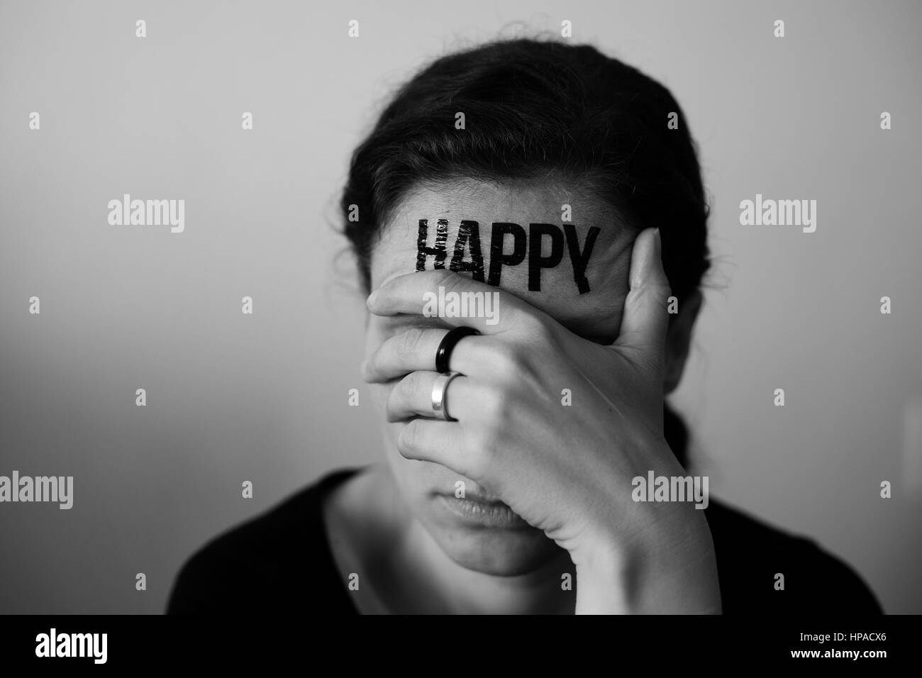 Head of a Woman with inscription Happy on the forehead, with hand over her eyes Stock Photo