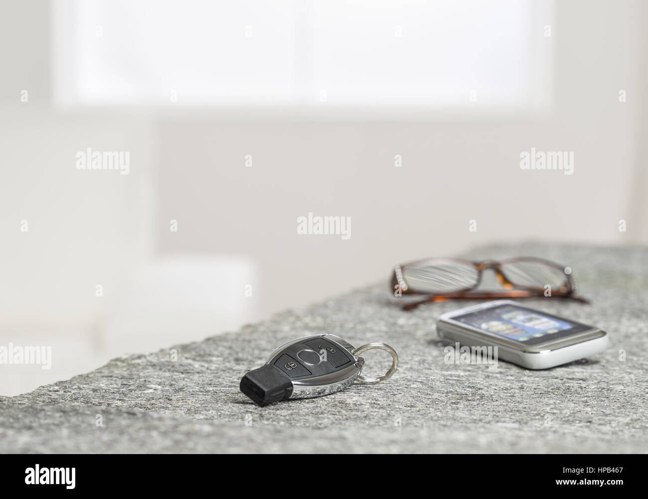Autoschluessel, Smartphone und Brille liegen auf einem Tisch Stock Photo