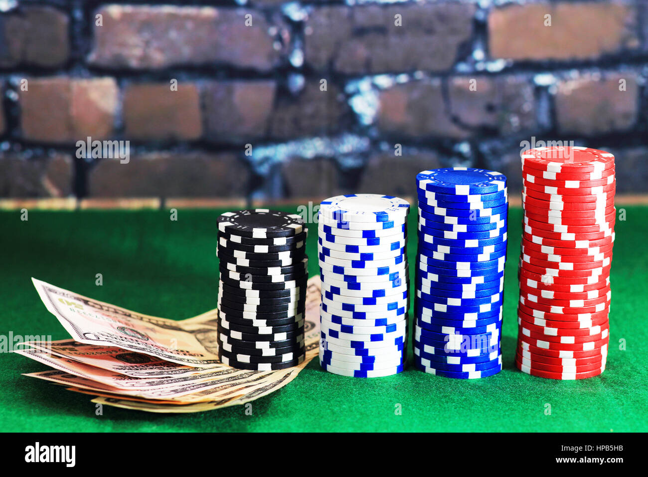 Casino chips and money on green poker table. Color poker chips in column form on brick wall background. Games of chance theme. Stock Photo