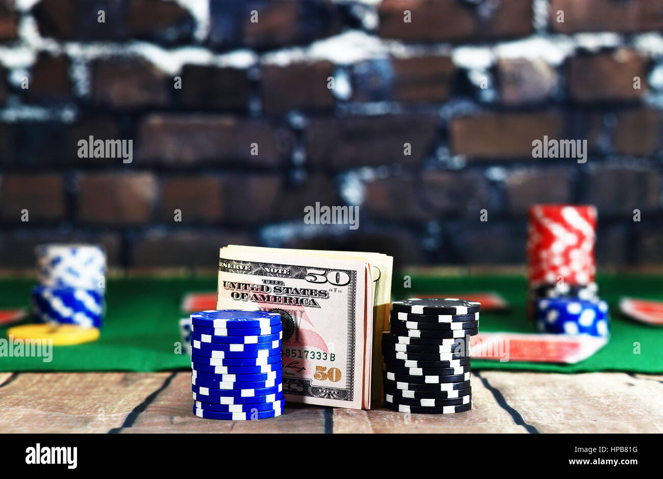 Close up of money between casino chips on poker play background. Dollars on wooden table on brick wall background. Online casino background. Stock Photo