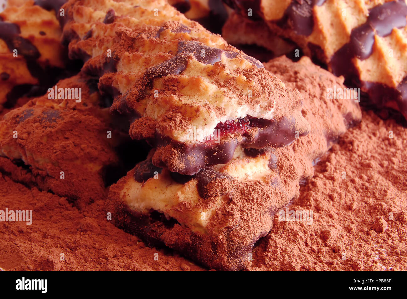 Pile of shortbread cookies with jam and chocolate icing on the scattered cocoa powder close up. Stock Photo