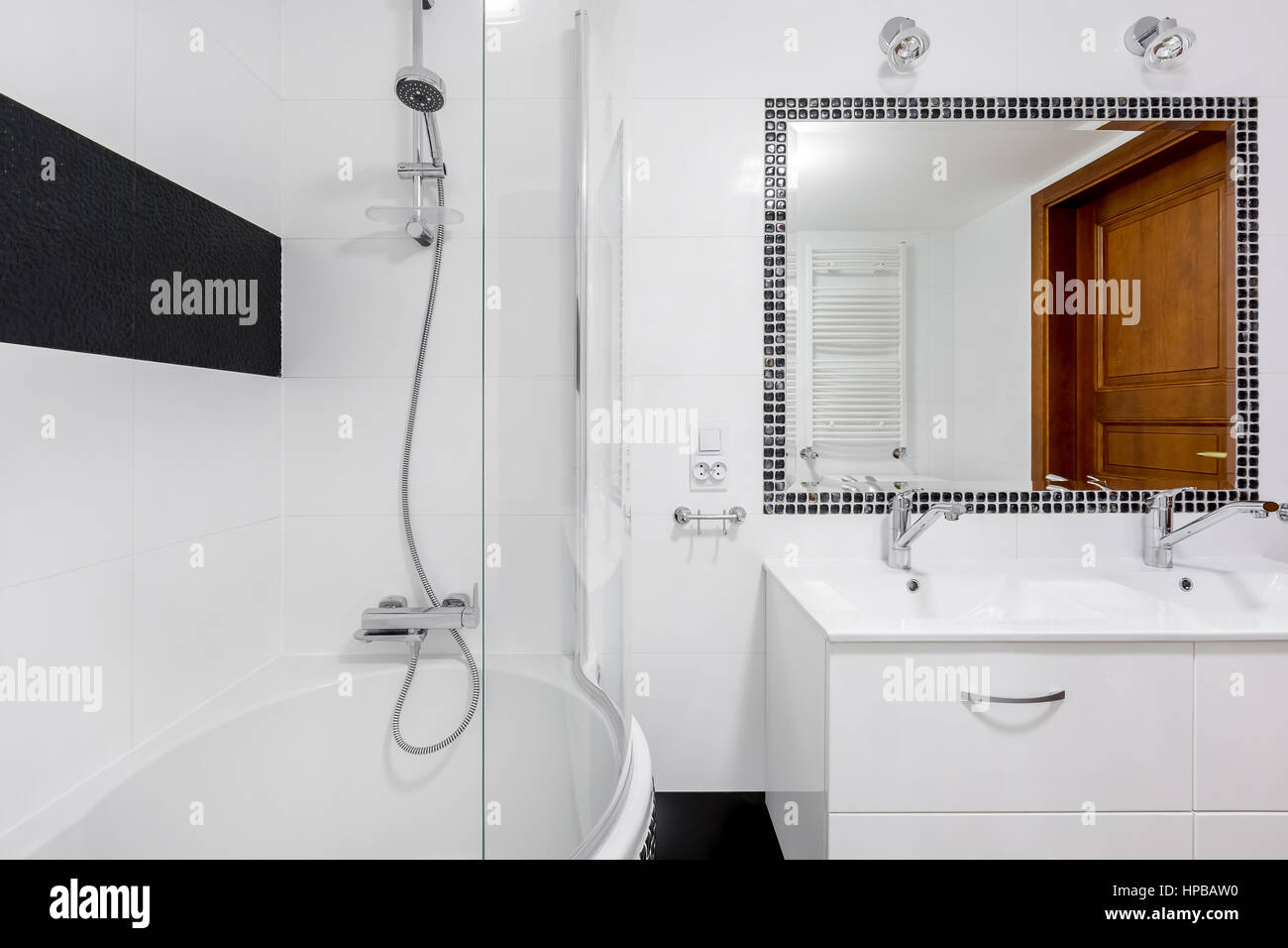 White luxury bathroom interior with big mirror, two faucets and bathtub with shower Stock Photo