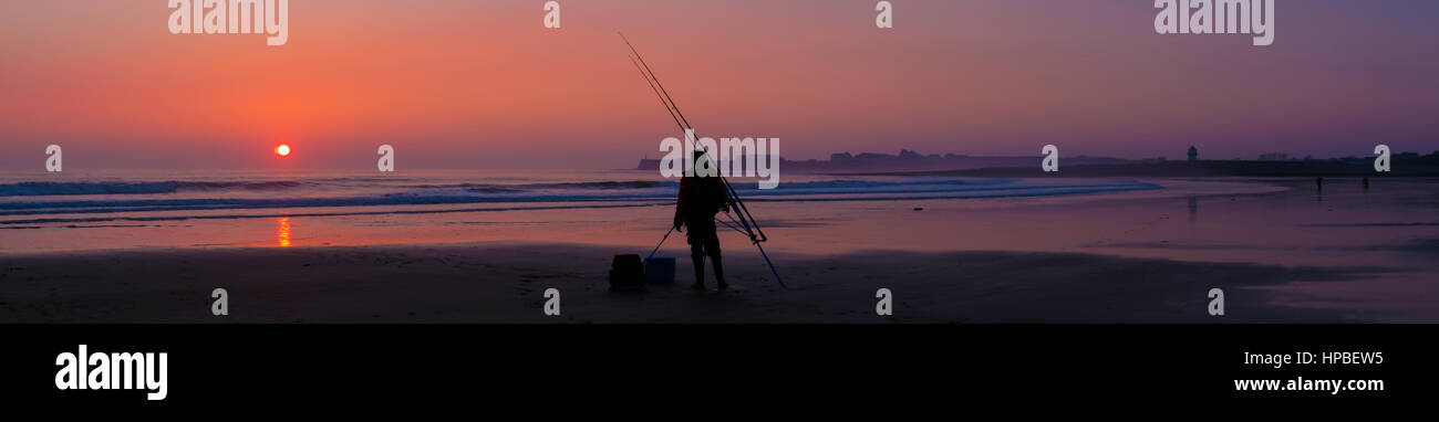 Catching A Sunset on The Beach At Trecco Bay Near Porthcawl In Wales. Alone Fisherman hoping for a catch as The Sunsets Stock Photo