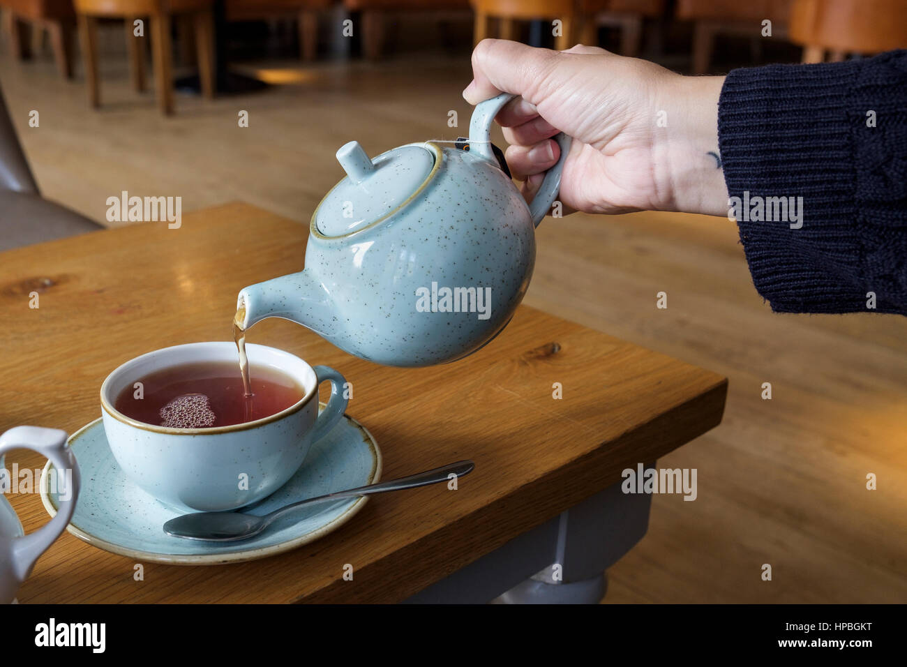 A woman in a cafe is pictured pouring tea from a blue teapot into a