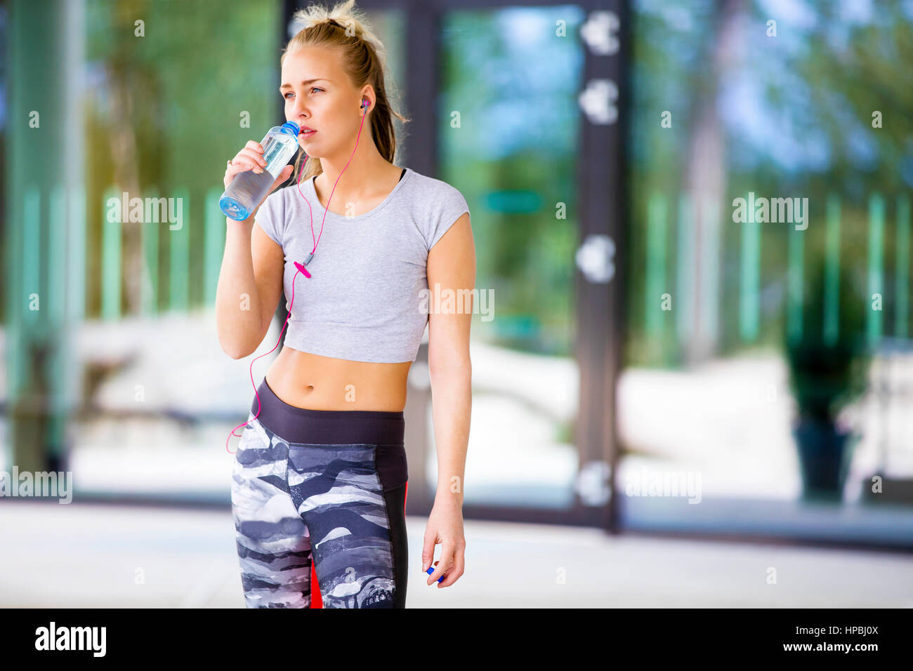 Tired young woman drinking water from bottle after workout outdoors Stock Photo