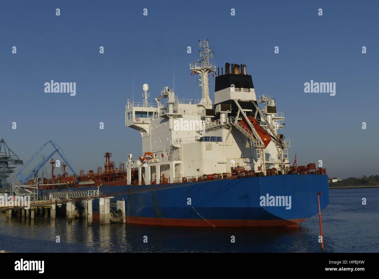 Products Tanker discharging at the Oil Terminal with blue hull and red main deck on sunny day. Stock Photo