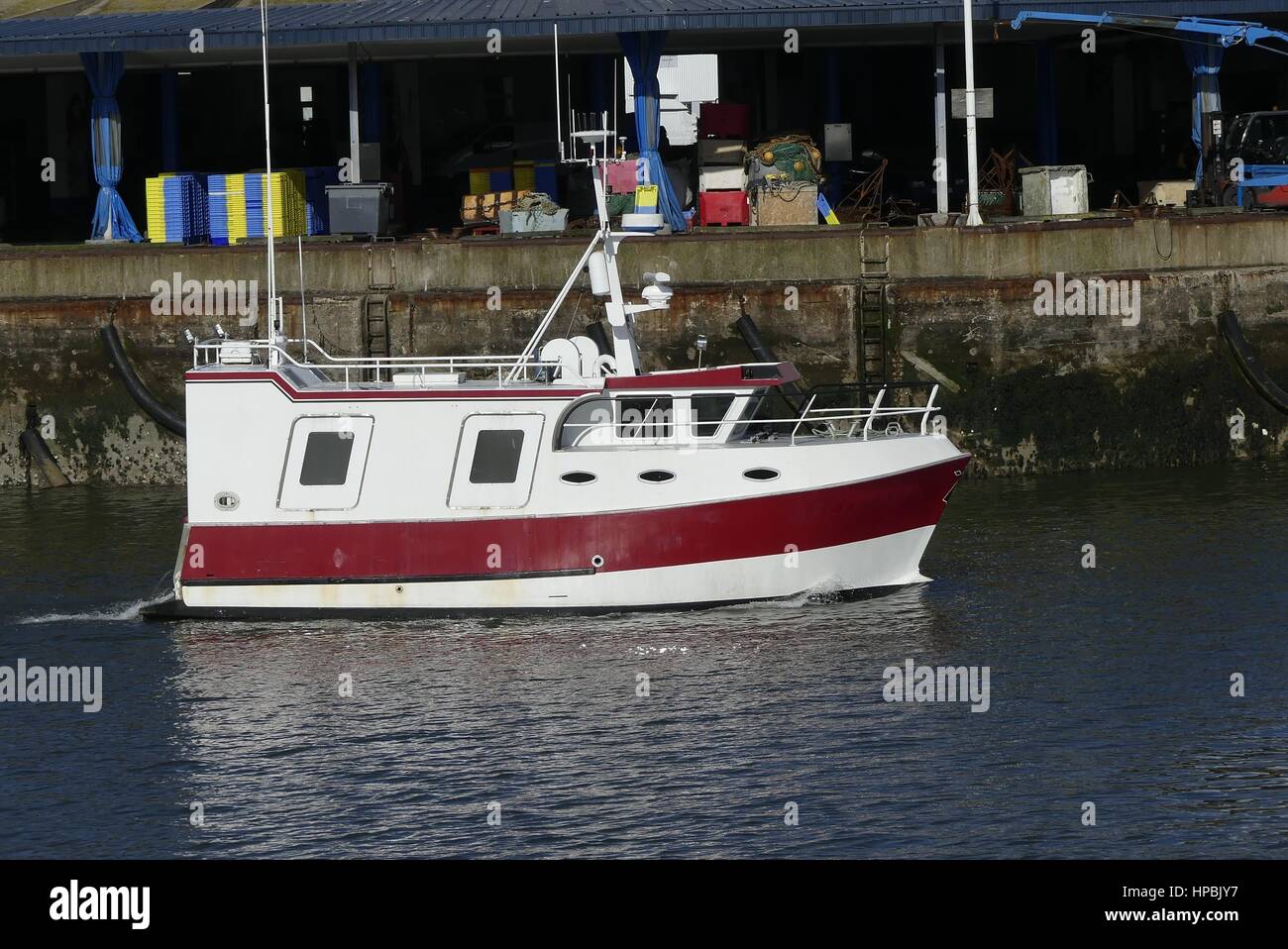 Red and white fishing boat underway in the harbor with pier and