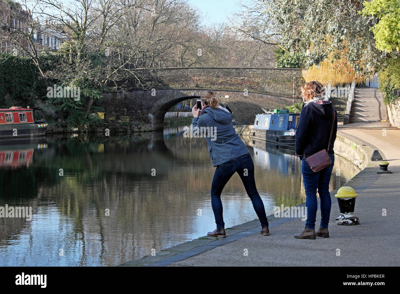 A woman tourist leaning to photograph bridge on City Road Basin area of Regents Canal in Islington, East London E1 England UK  KATHY DEWITT Stock Photo