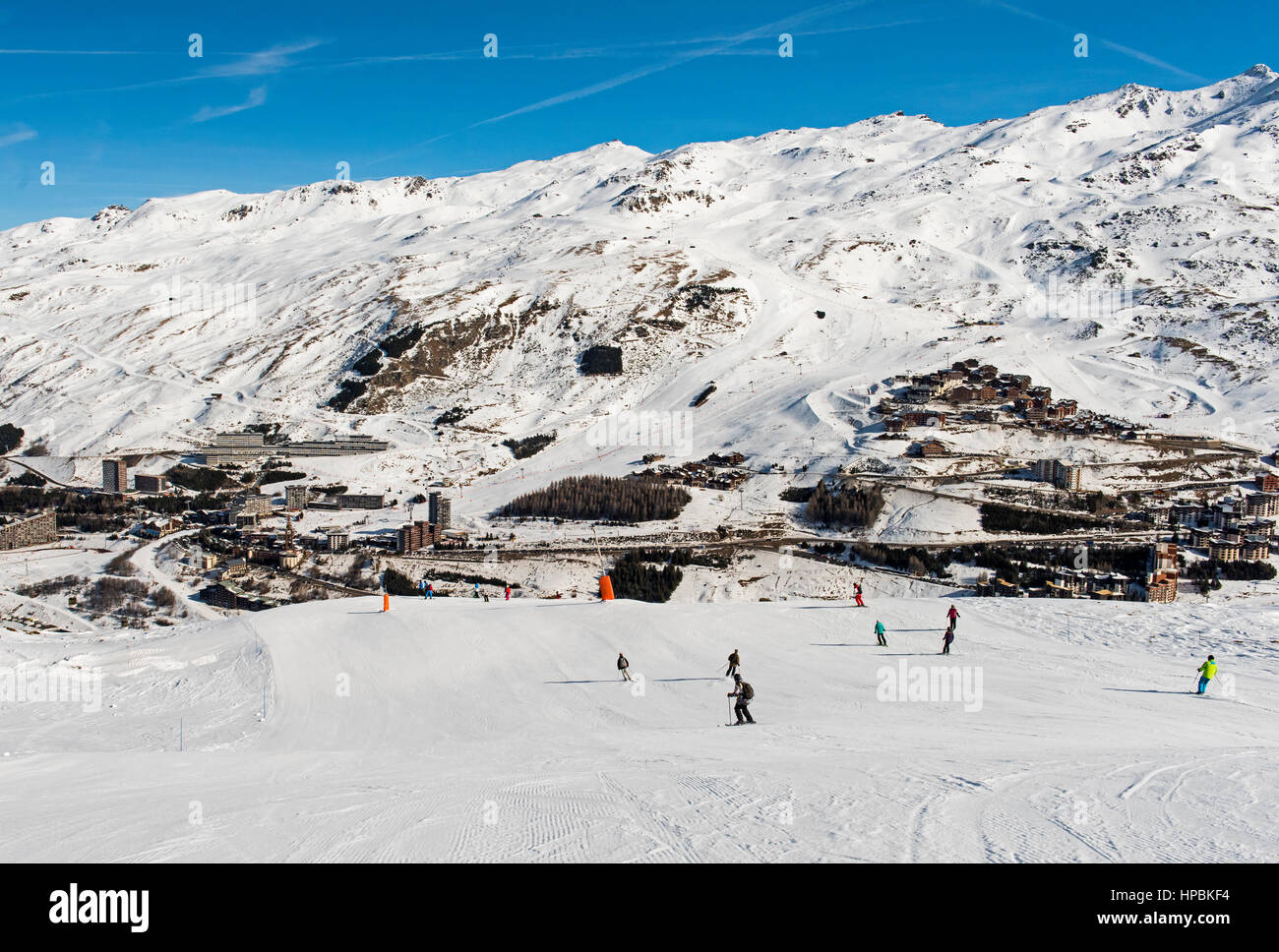 Skiers on a ski slope piste at winter alpine mountain resort with village in background Stock Photo
