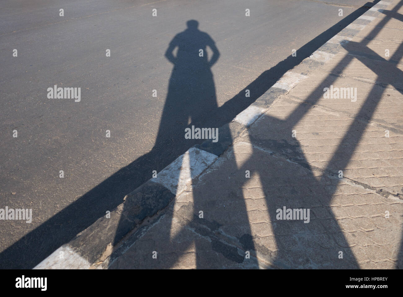 Indian man taking a picture of his own shadow standing on a sidewalk next to railing in Hyderabad,India Stock Photo