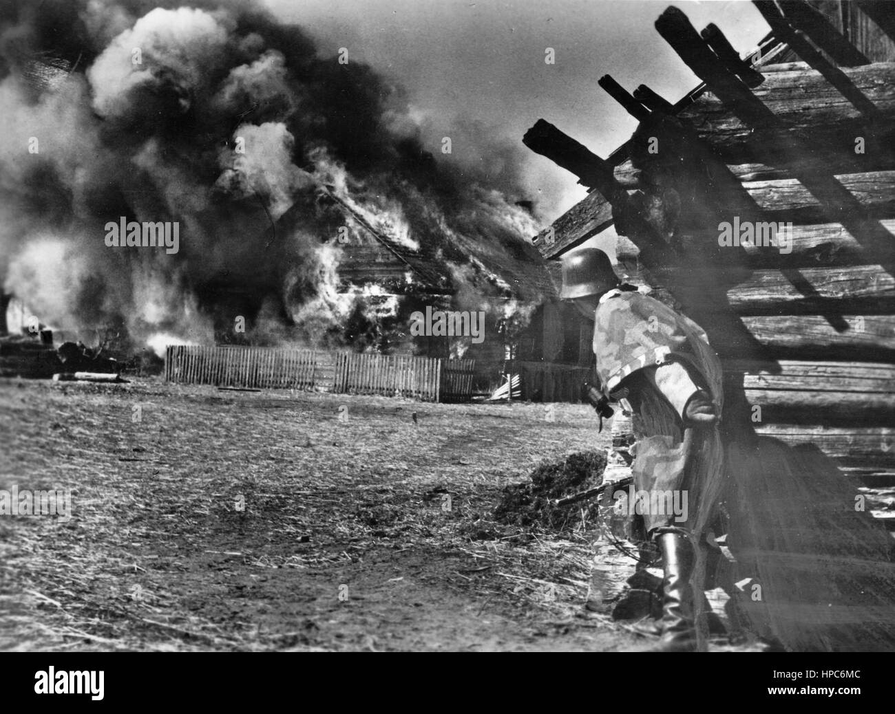 The Nazi Propaganda! on the back of the image reads: 'Bandits are smoked out. SS grenadiers again caught a Bolshevist gang in one of the villages which belong to their base. The gang nests each are encircled and while some of the grenadiers secure the area with the IMG, others work their way towards the houses on fire. Heavy explosions show that a great amount of ammunition was stored in this gang nest.' Image from the Eastern Front/Russia, 21 July 1943. Since the summer of 1942, the German were not allowed to use the term 'partisans' anymore for psychological reasons. Instead, terms like 'gan Stock Photo
