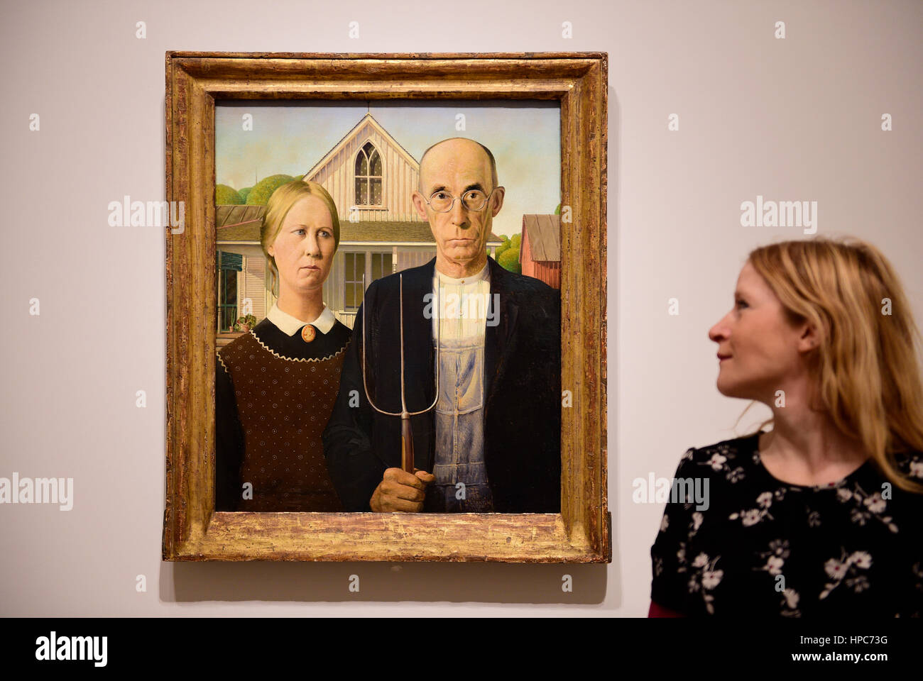 Royal Academy, London, UK. 21st Feb, 2017. America after the Fall: Painting in the 1930's, an exhibition chronicling the turbulent economic and political climate dominating the decade after the Wall Street Crash of 1929. Included in the exhibition is the iconic painting ‘American Gothic' by Grant Wood (photo), posed with a member of gallery staff, seen outside of America for the very first time, and works by Edward Hopper, Georgia O'Keefe, Jackson Pollock and Thomas Hart Benton. Credit: Malcolm Park editorial/Alamy Live News Stock Photo