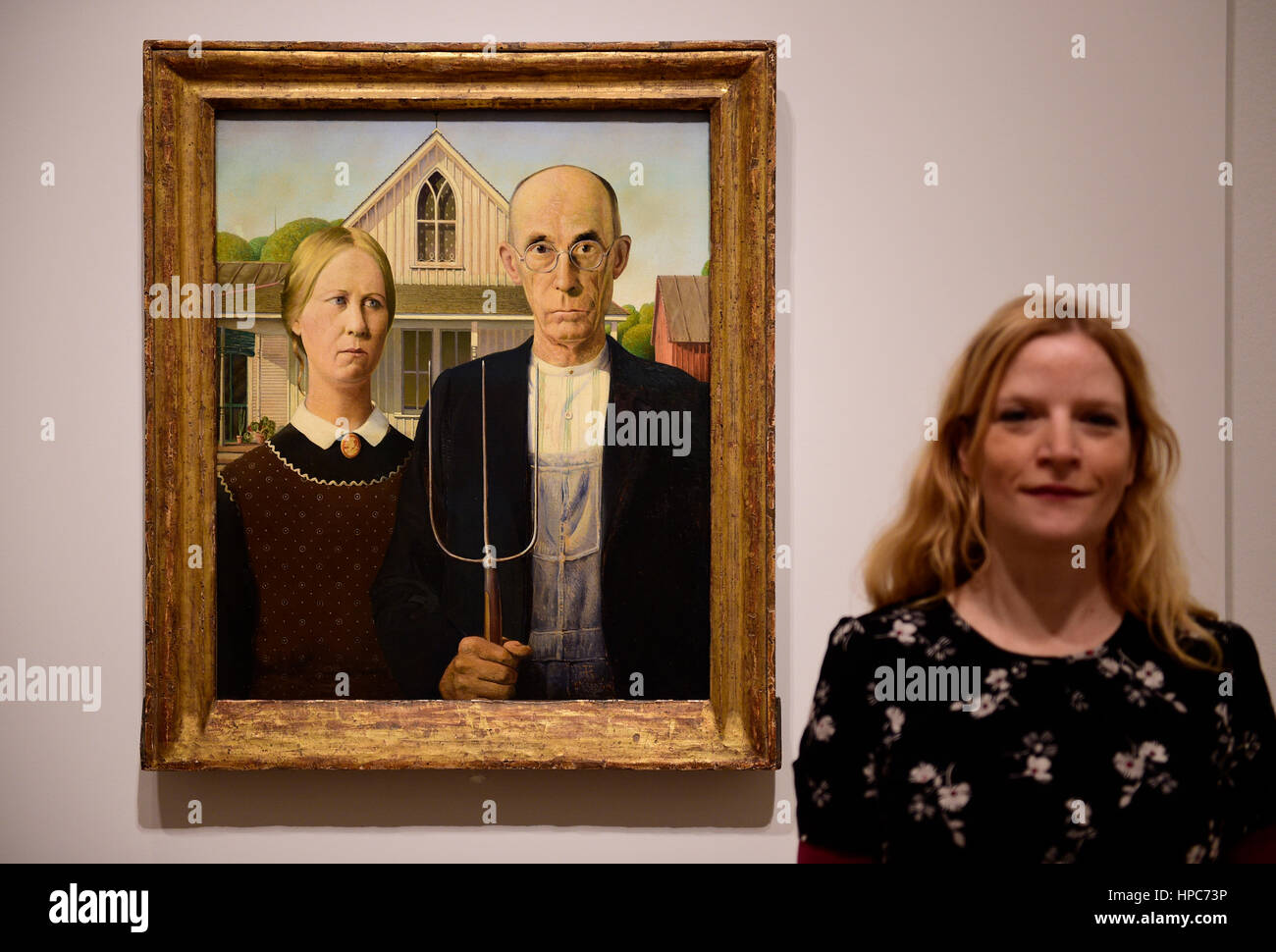 Royal Academy, London, UK. 21st Feb, 2017. America after the Fall: Painting in the 1930's, an exhibition chronicling the turbulent economic and political climate dominating the decade after the Wall Street Crash of 1929. Included in the exhibition is the iconic painting ‘American Gothic' by Grant Wood (photo), posed with a member of gallery staff, seen outside of America for the very first time, and works by Edward Hopper, Georgia O'Keefe, Jackson Pollock and Thomas Hart Benton. Credit: Malcolm Park editorial/Alamy Live News Stock Photo