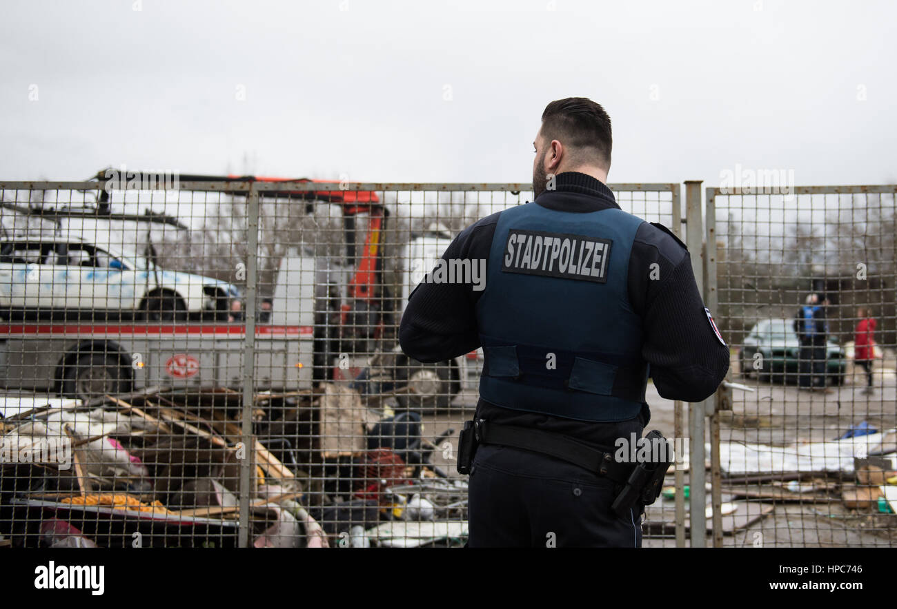 A state police officer stands in front of the fence at a commercial property while a tow truck tows away a rusty car in the Gutleutviertel district on the outskirts of Frankfurt am Main, Germany, 21 February 2017. The handbuilt huts of the property's residents have been torn down. Several dozen Romanians were living in the wooden sheds. Photo: Susann Prautsch/dpa Stock Photo