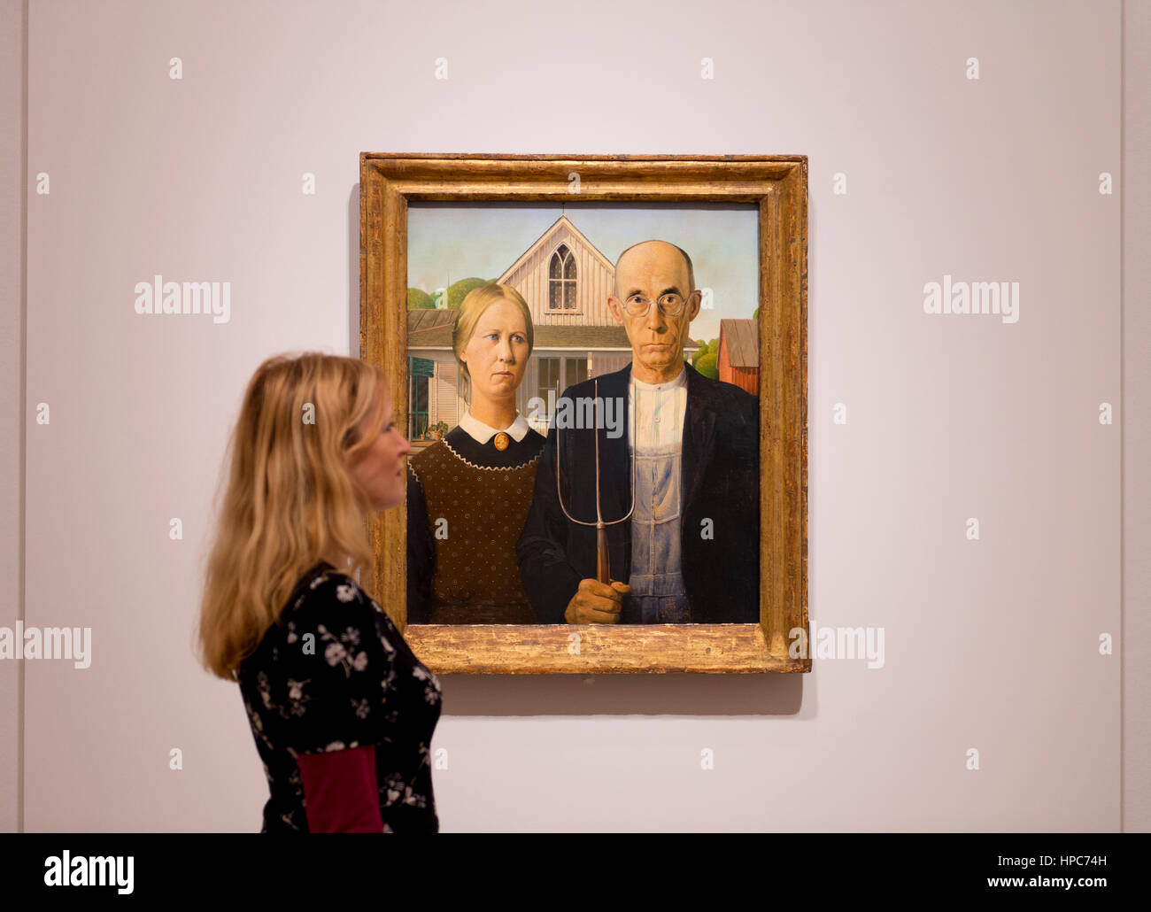 Royal Academy, London, UK. 21st Feb, 2017. America after the Fall: Painting in the 1930's, an exhibition chronicling the turbulent economic and political climate dominating the decade after the Wall Street Crash of 1929. Included in the exhibition is the iconic painting ‘American Gothic' by Grant Wood (photo), posed with a member of gallery staff, seen outside of America for the very first time, and works by Edward Hopper, Georgia O'Keefe, Jackson Pollock and Thomas Hart Benton. Credit: Malcolm Park editorial/Alamy Live News Stock Photo