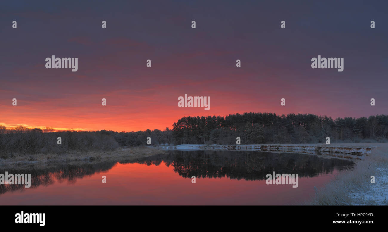 Autumn sunrise over lake. Bright red clouds above water. Panoramic view. Stock Photo