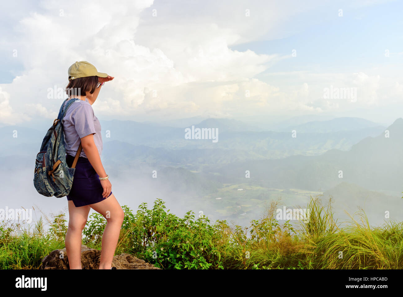 Traveler teens girl hiker wear cap and glasses with backpack looking beautiful nature landscape on high mountain at viewpoint of Phu Chi Fa Stock Photo