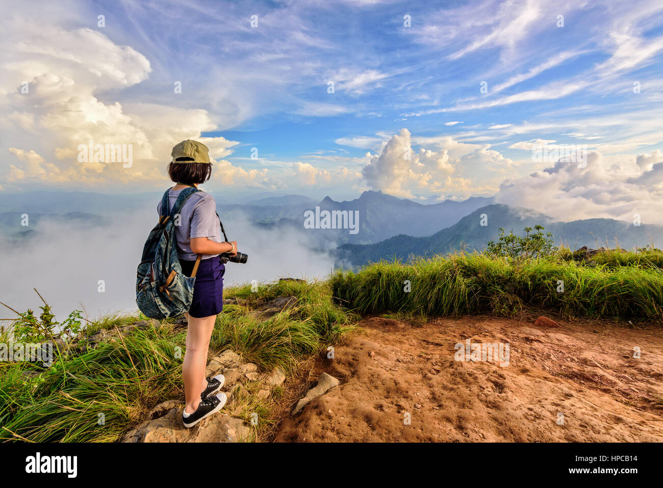 Hiker asian teens girl with camera and backpack wear caps and glasses looking beautiful landscape nature of mountain range and blue sky during sunset  Stock Photo