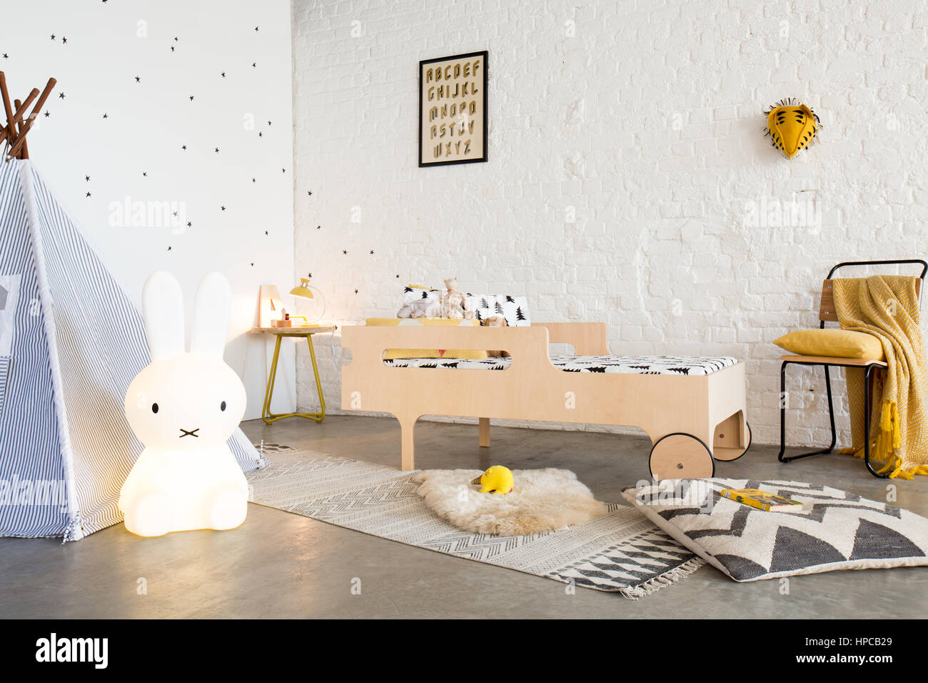 A child's bed in a white bedroom with poured concrete floor a teepee and a white brick wall Stock Photo