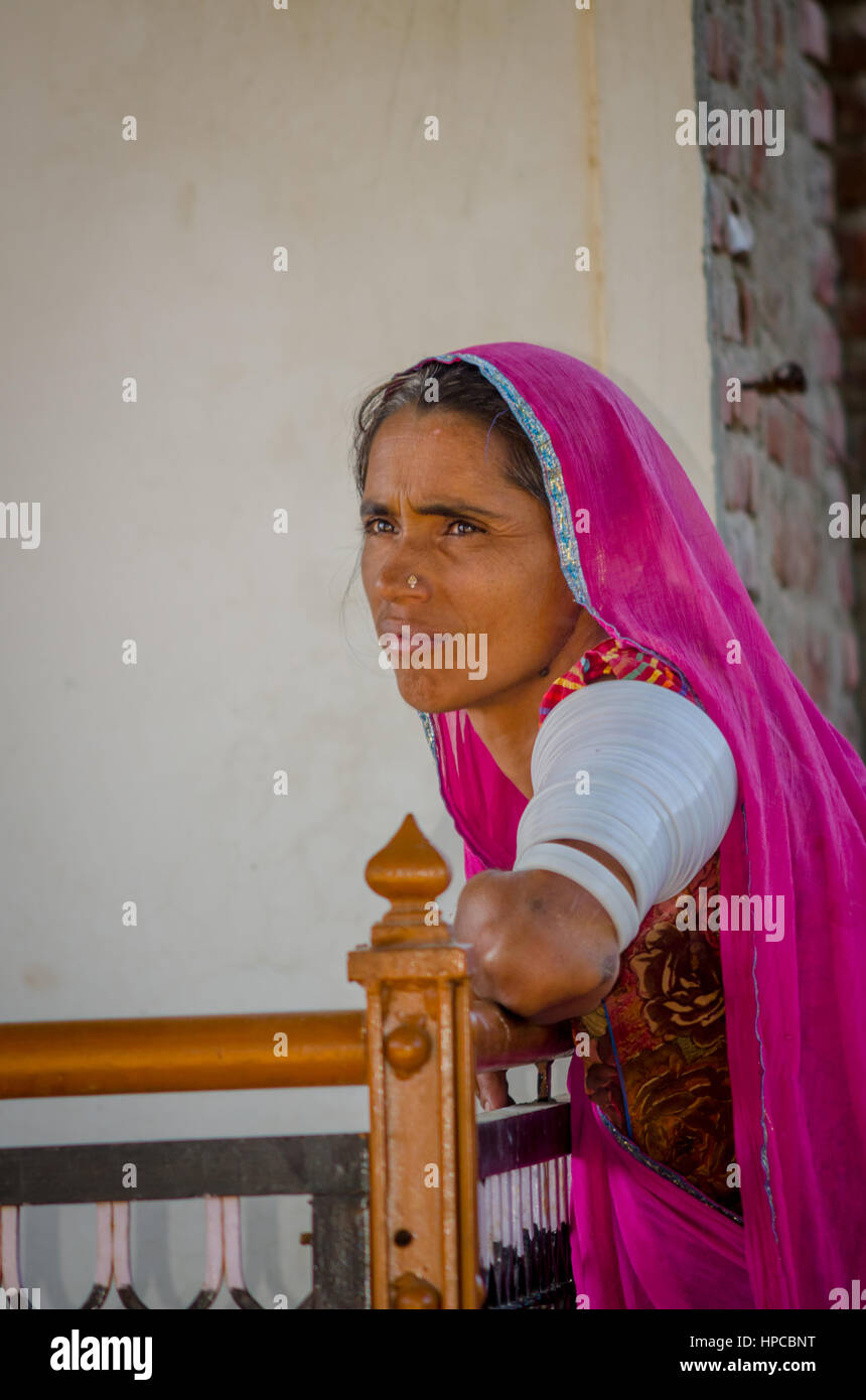 RAJASTHAN, INDIA - NOVEMBER 20, 2016: Unidentified elderly Rajasthani woman waiting for someone wearing traditional costume and red sari with ornament Stock Photo
