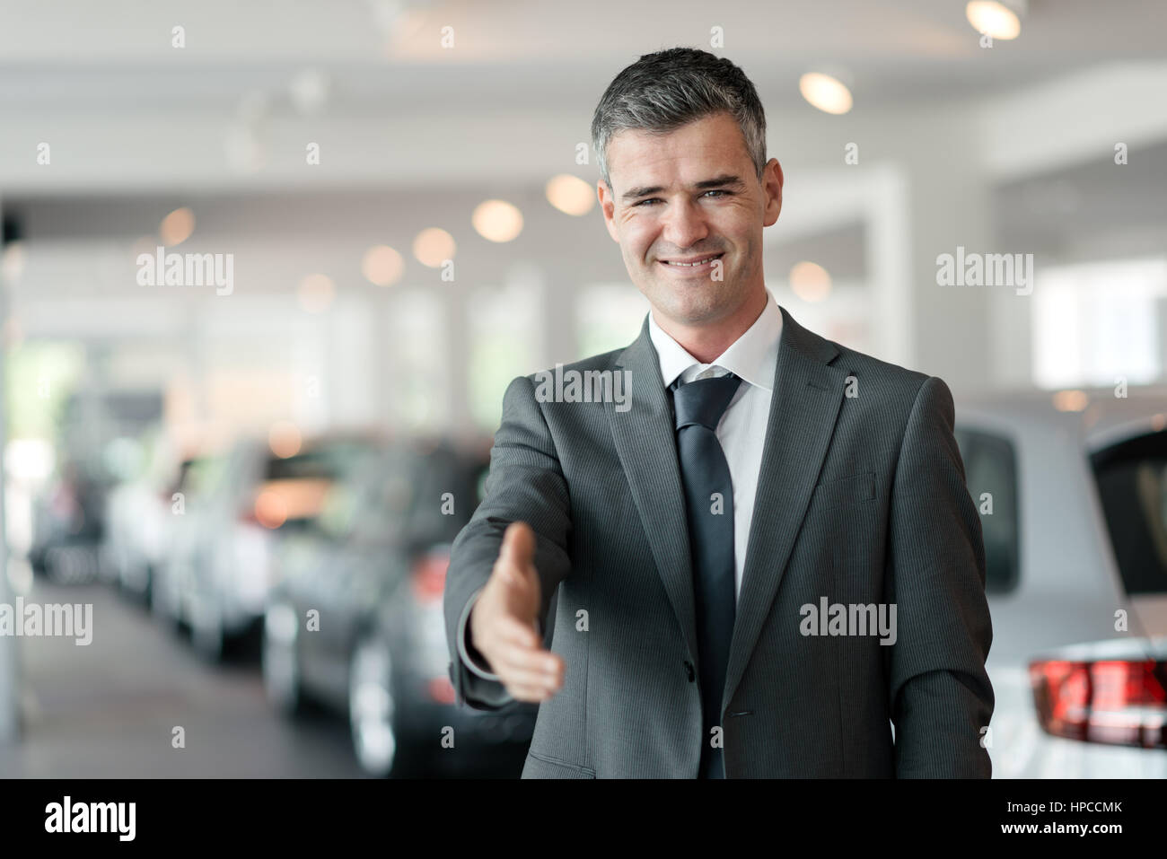Confident car dealer giving a handshake, car showroom on the background Stock Photo