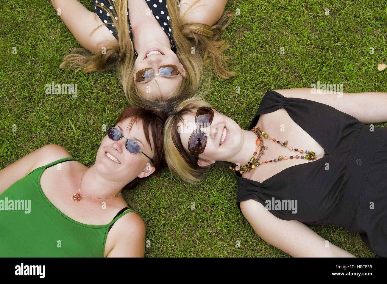Model released , Drei Frauen mit Sonnenbrillen liegen Kopf an Kopf in der Wiese - women lying in the meadow Stock Photo