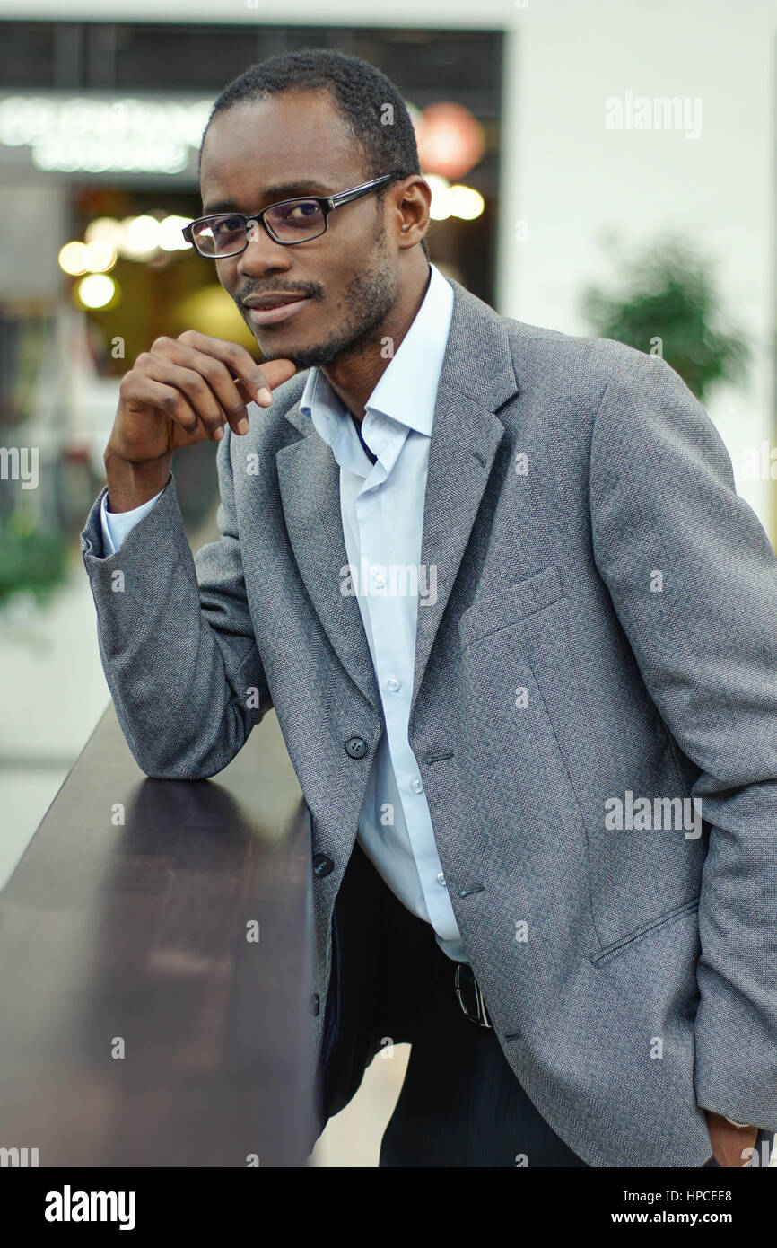 Portrait of young afro american man in a grey suit and glasses standing ...