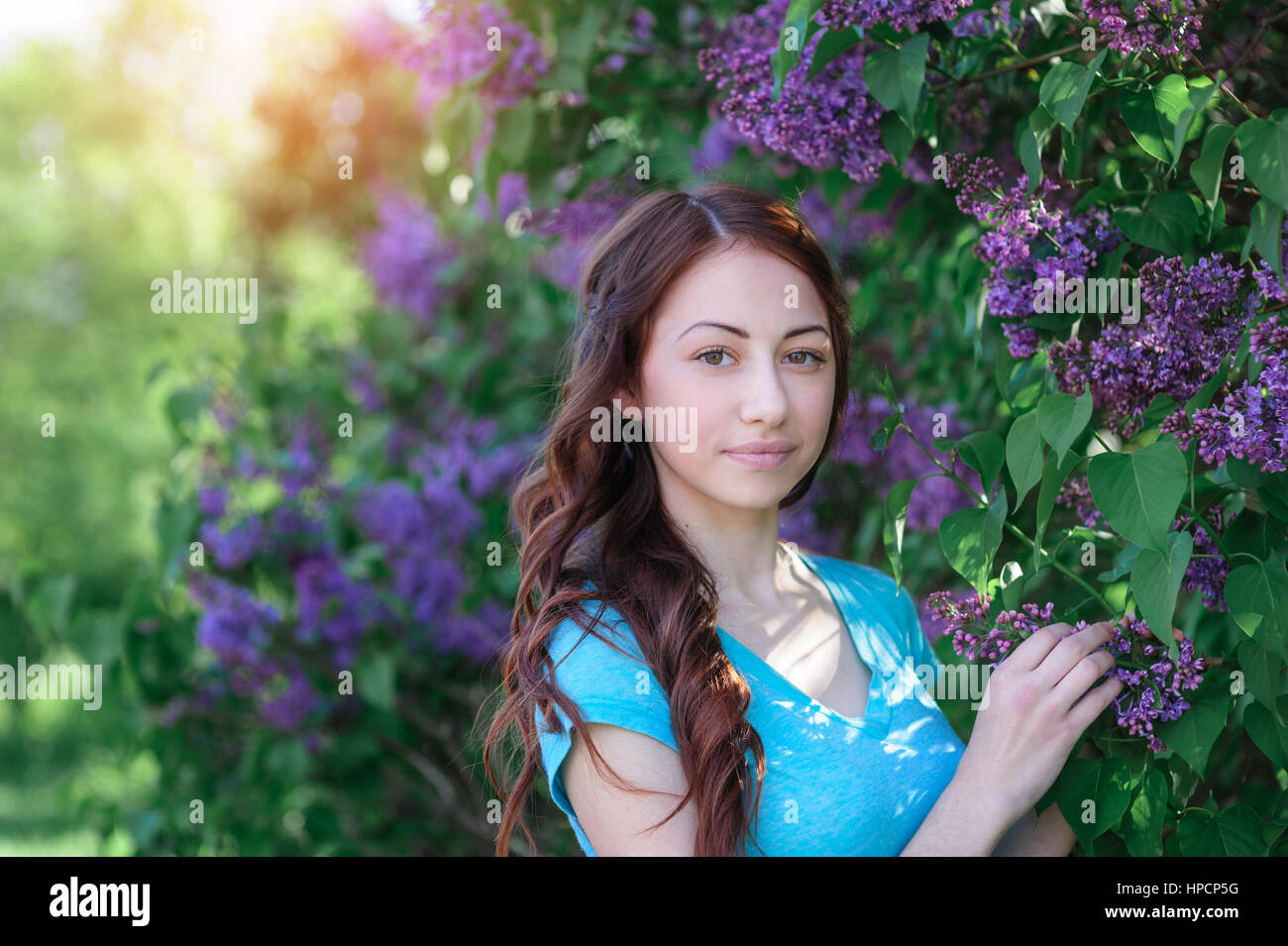young woman near the lilac bush in the spring park. Stock Photo