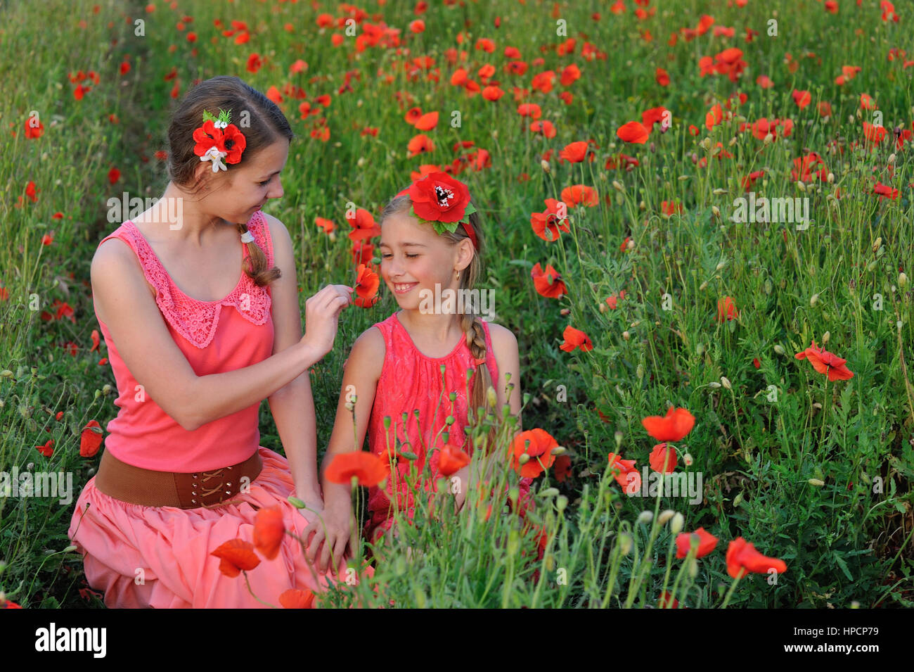 two girls in a red dress walking on the poppy field in Spring Stock ...
