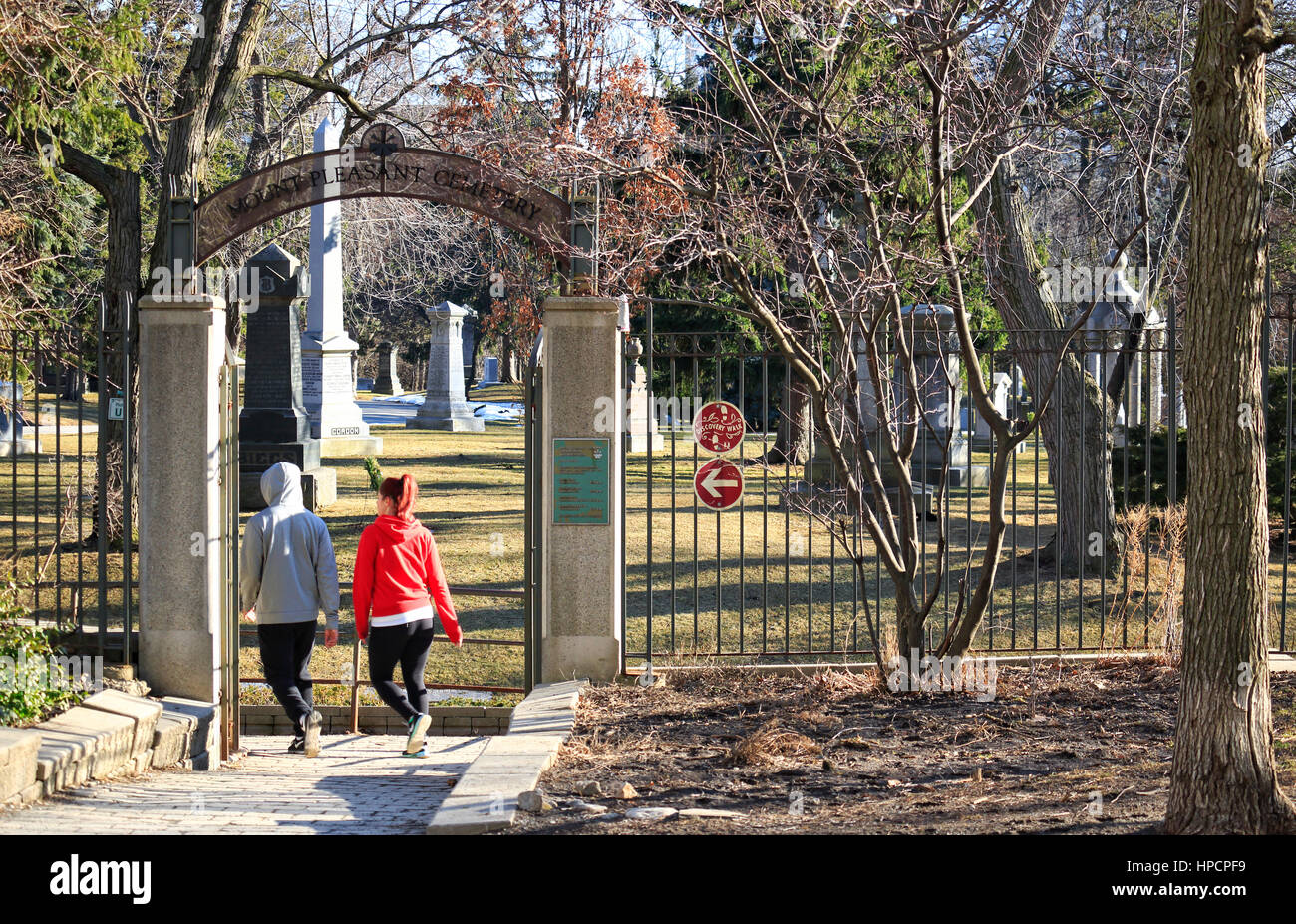 Two yonge persons walking briskly on Disvery Walk into historic Mount Pleasant Cemetery from Beltline Trail in Toronto, Ontario, Canada, on a sunny da Stock Photo