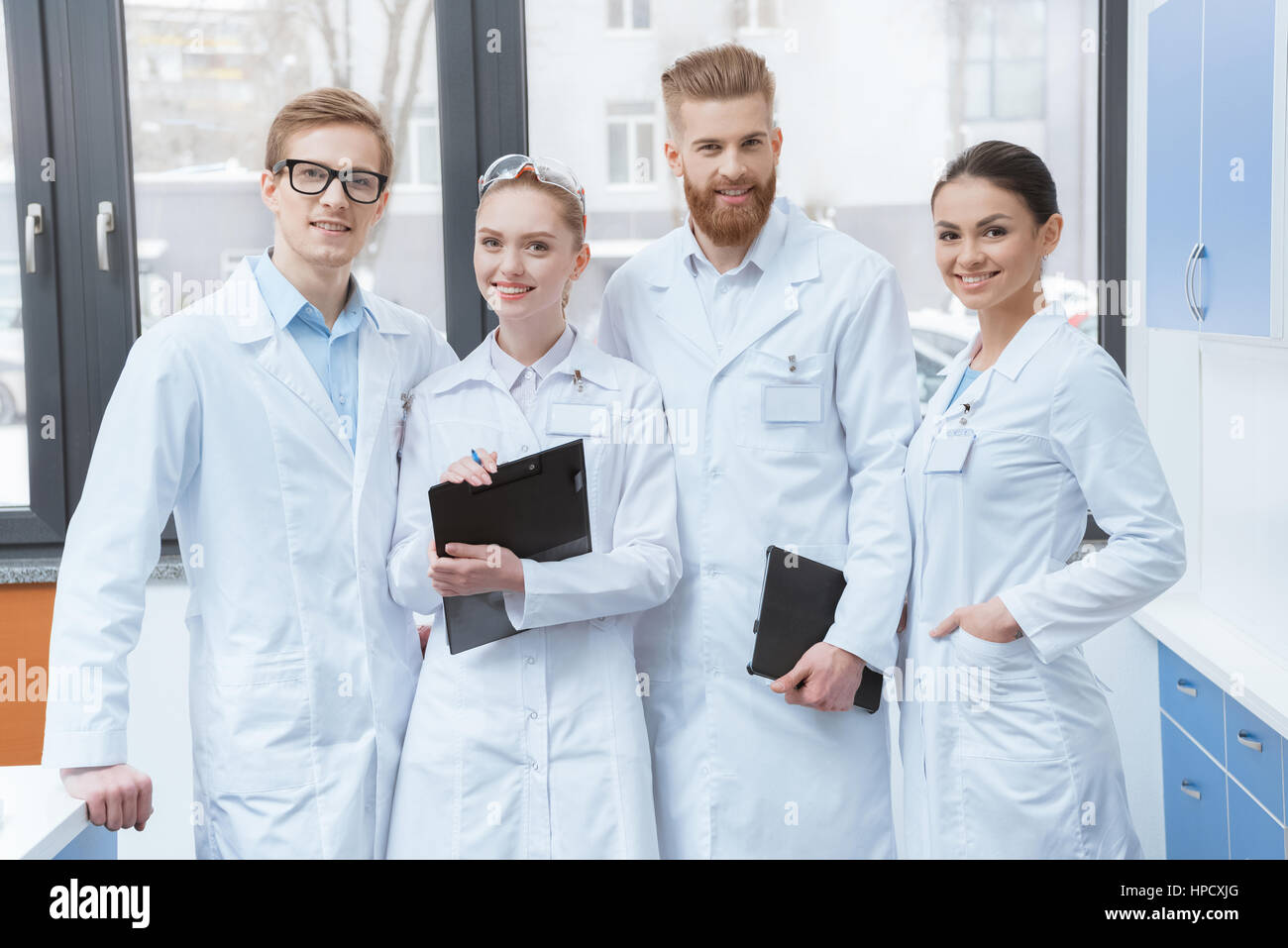 Team of young professional scientists in white coats smiling at camera